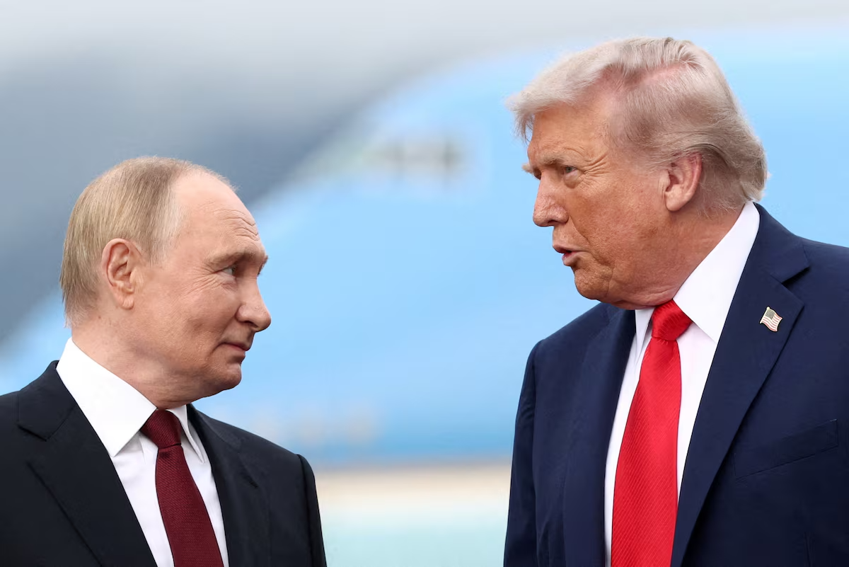 Donald Trump, wearing a navy suit and red tie, speaks to Vladimir Putin, wearing a black suit and burgundy tie, as they face each other during their August 15, 2025, meeting at Joint Base Elmendorf-Richardson in Anchorage, Alaska.