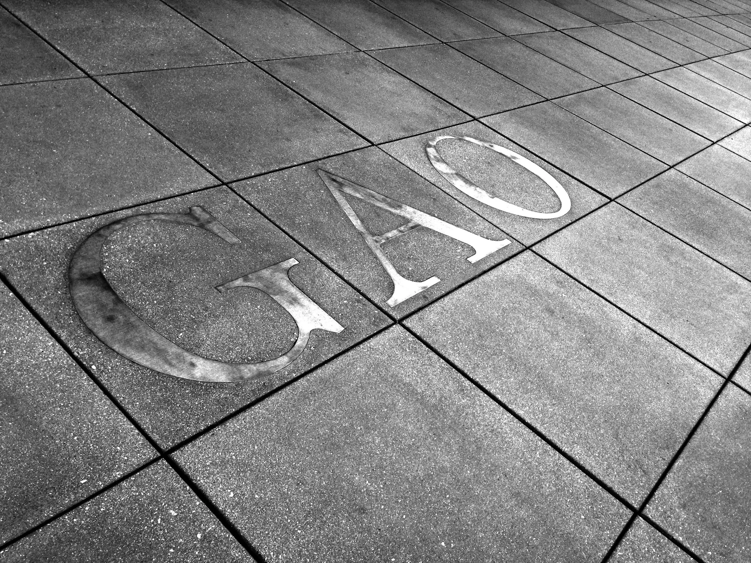 Large metal letters spelling “GAO” embedded in the paved walkway outside the Government Accountability Office.