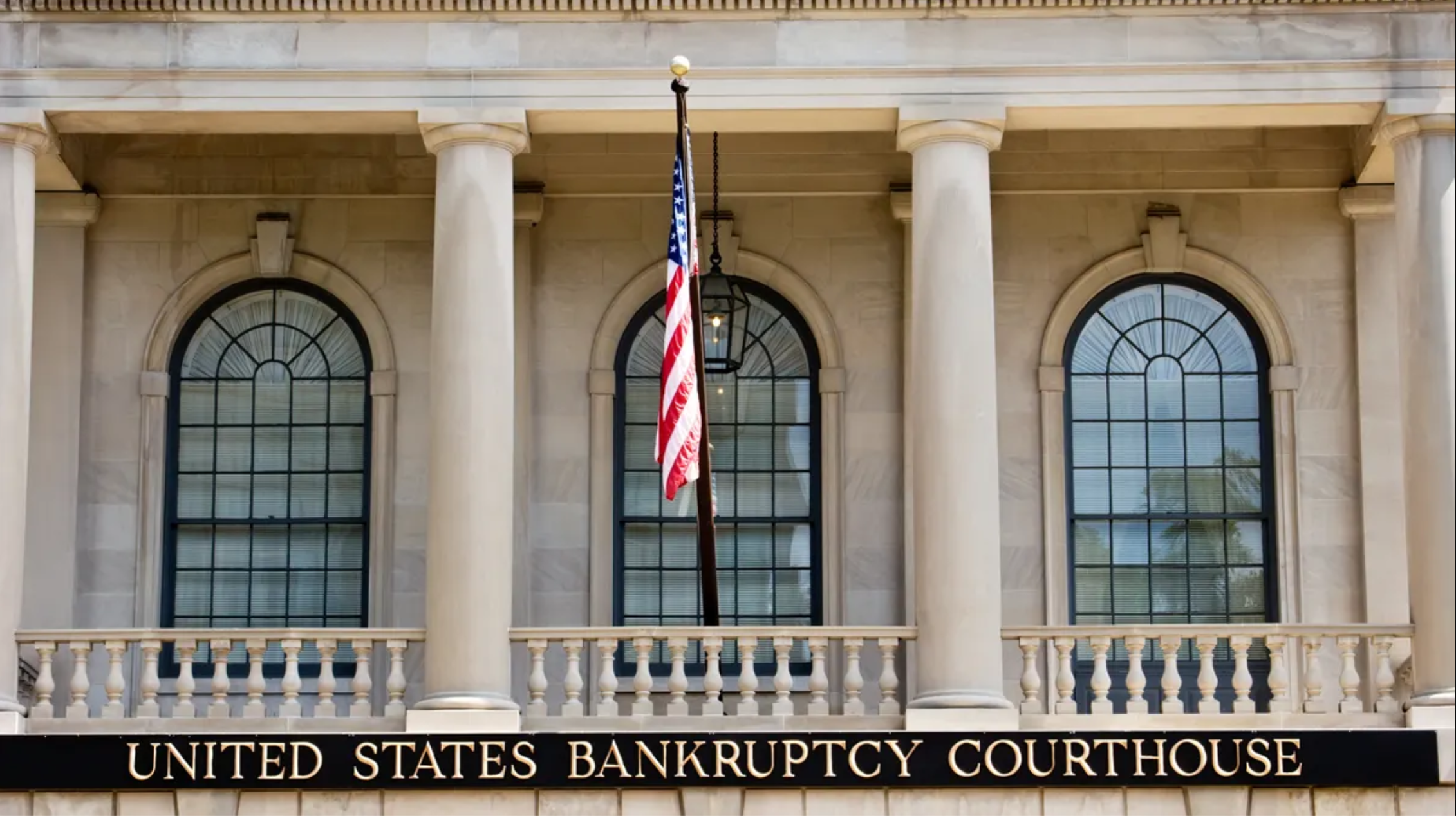 Exterior of a United States Bankruptcy Courthouse, showing its columns, windows, American flag, and identifying signage.