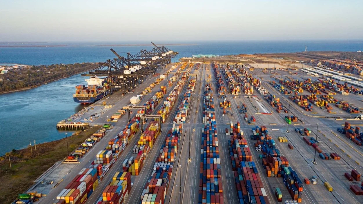 Aerial view of a container terminal at the Port of Houston, with rows of shipping containers, cargo cranes and a container ship docked alongside the terminal.