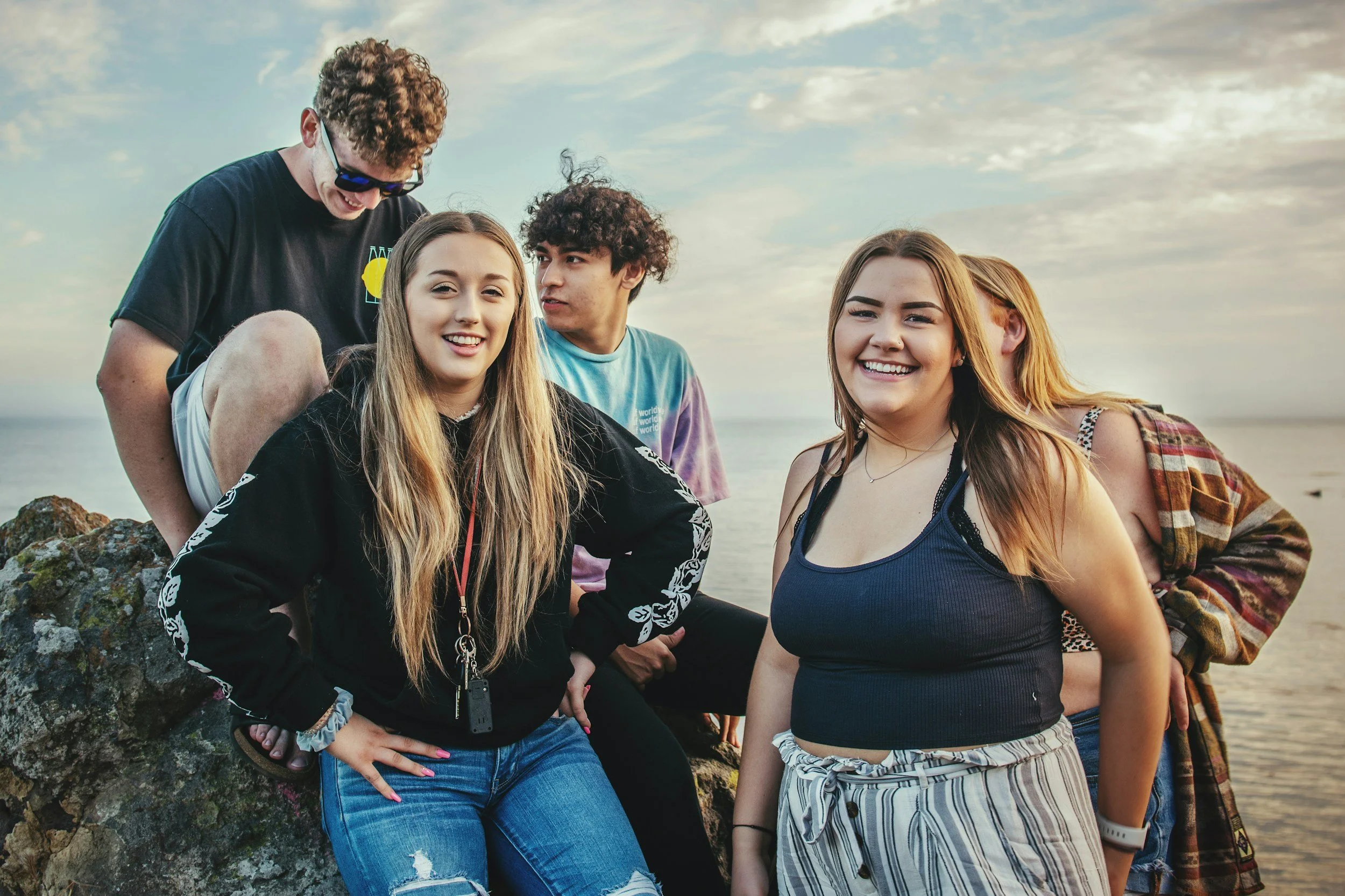 Groupe de jeunes amis se tenant près de la mer lors d'une journée ensoleillée, souriant et posant pour la photo.