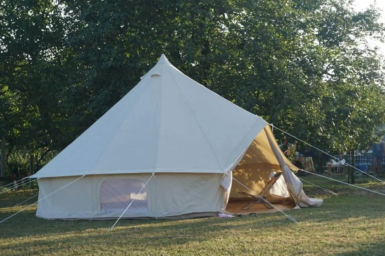 Large white canvas tent set up outdoors on grassy area with trees in background.