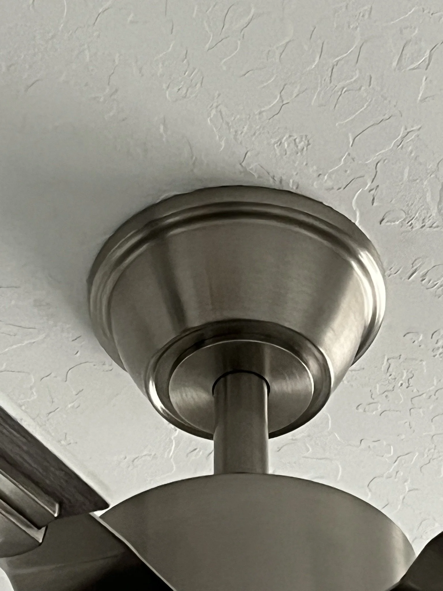 Close-up of a brushed nickel ceiling fan mount on a textured white ceiling.