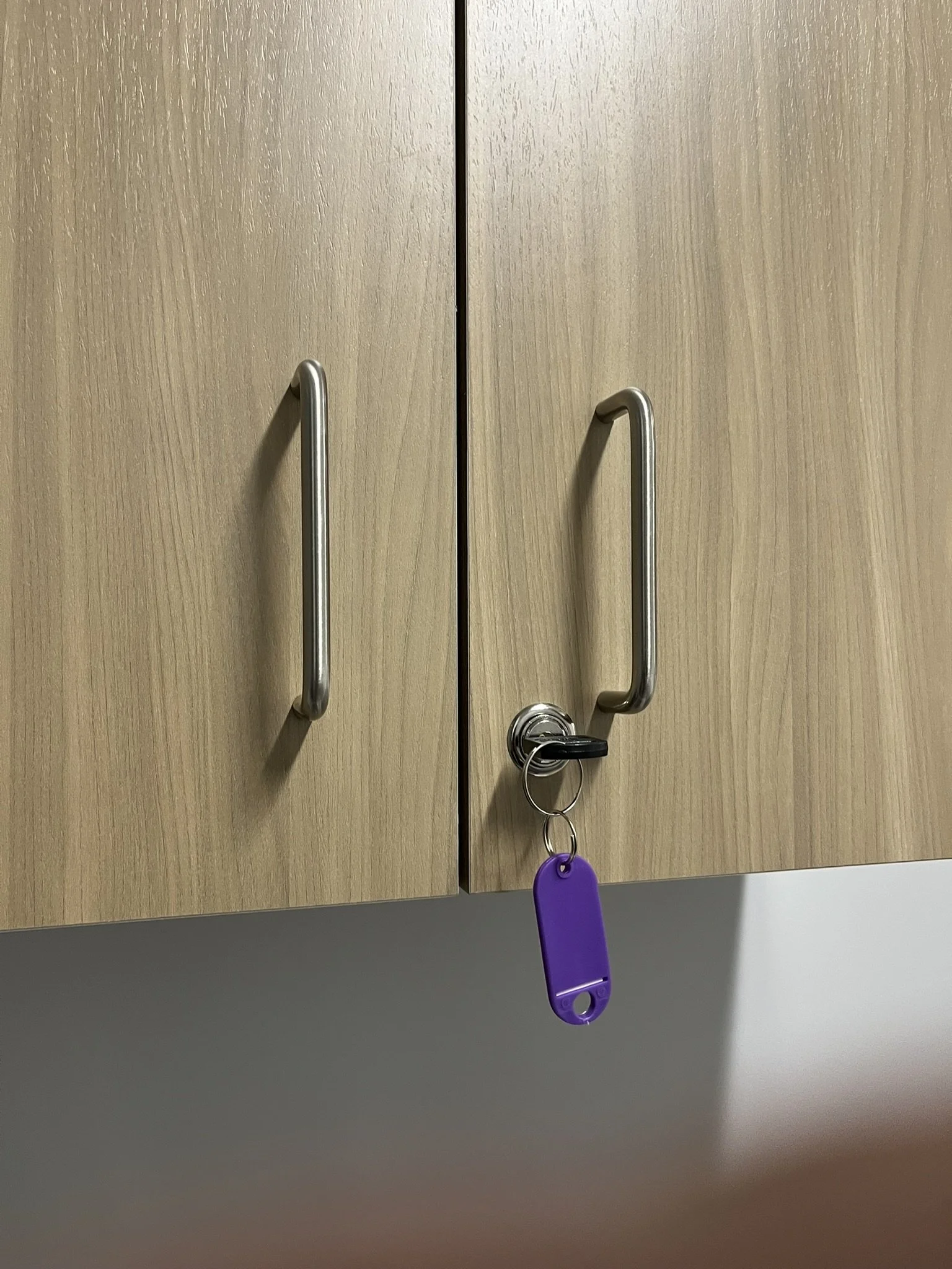 Wooden cabinet doors with metal handles, one door has a key with a purple keychain inserted in the lock.