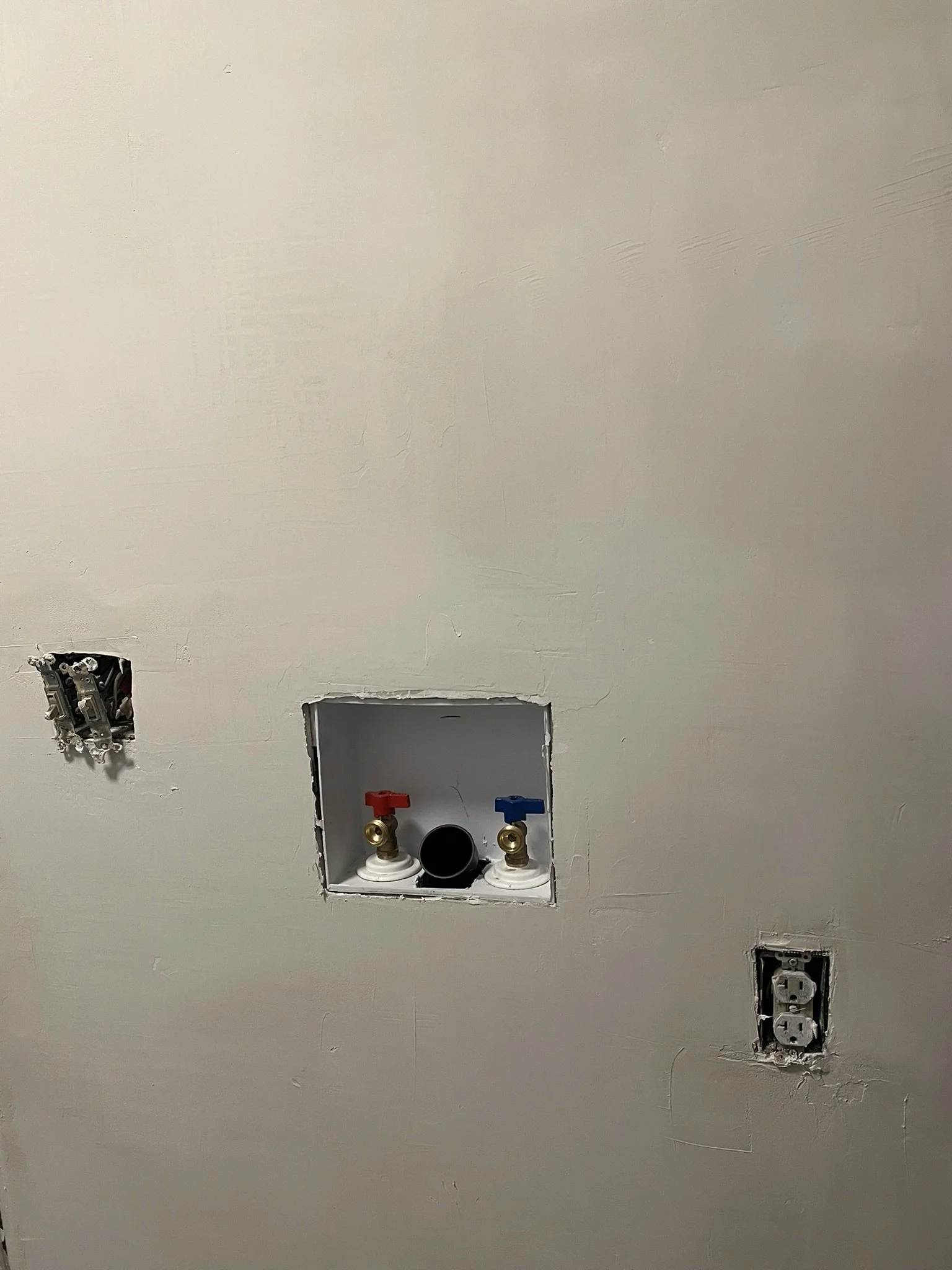 A wall with electrical outlets and a laundry hookup with water supply valves. level 5 drywall finish