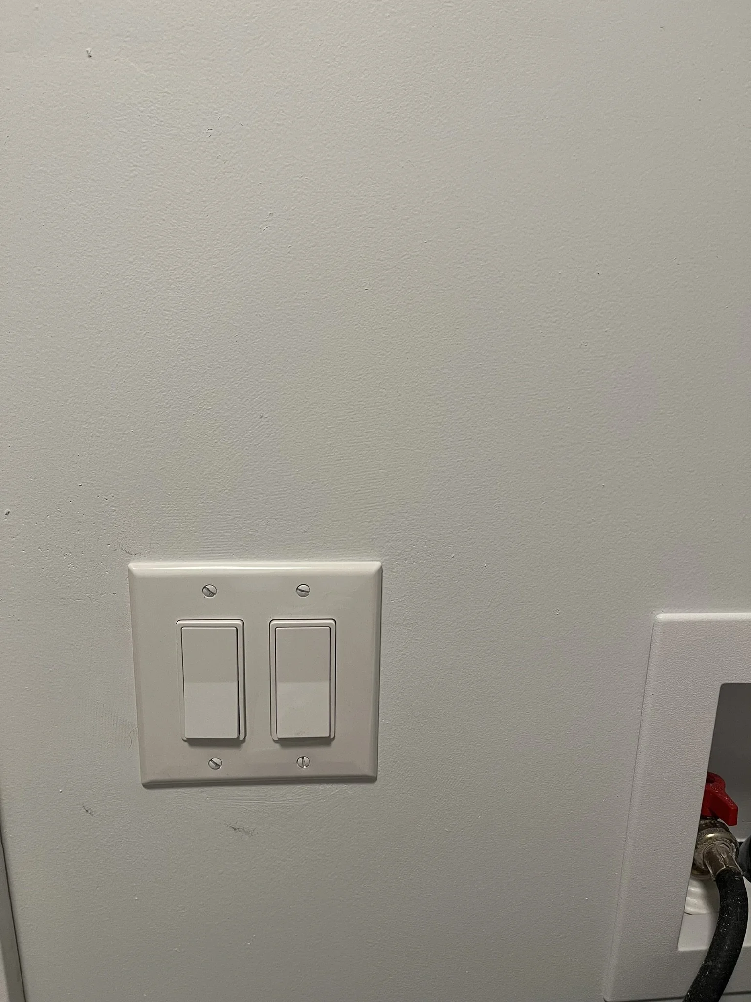 A white electrical wall panel with two switches and an adjacent outlet with a black hose connected.