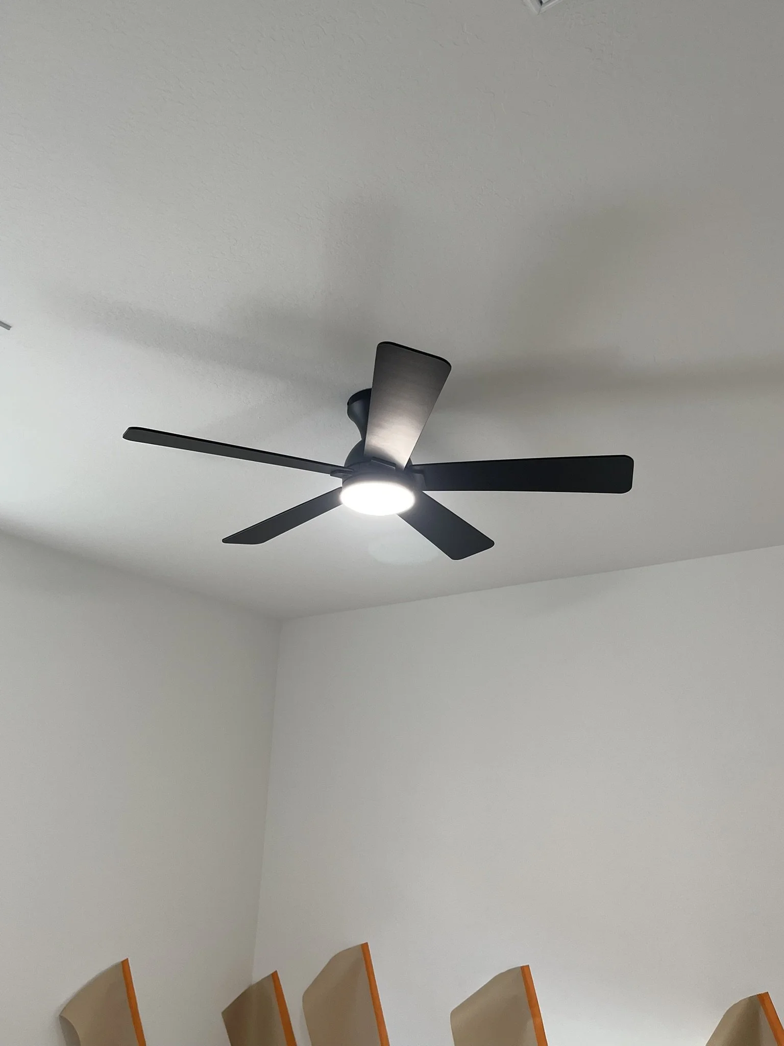 Black ceiling fan with five blades and a built-in light fixture on a white ceiling.