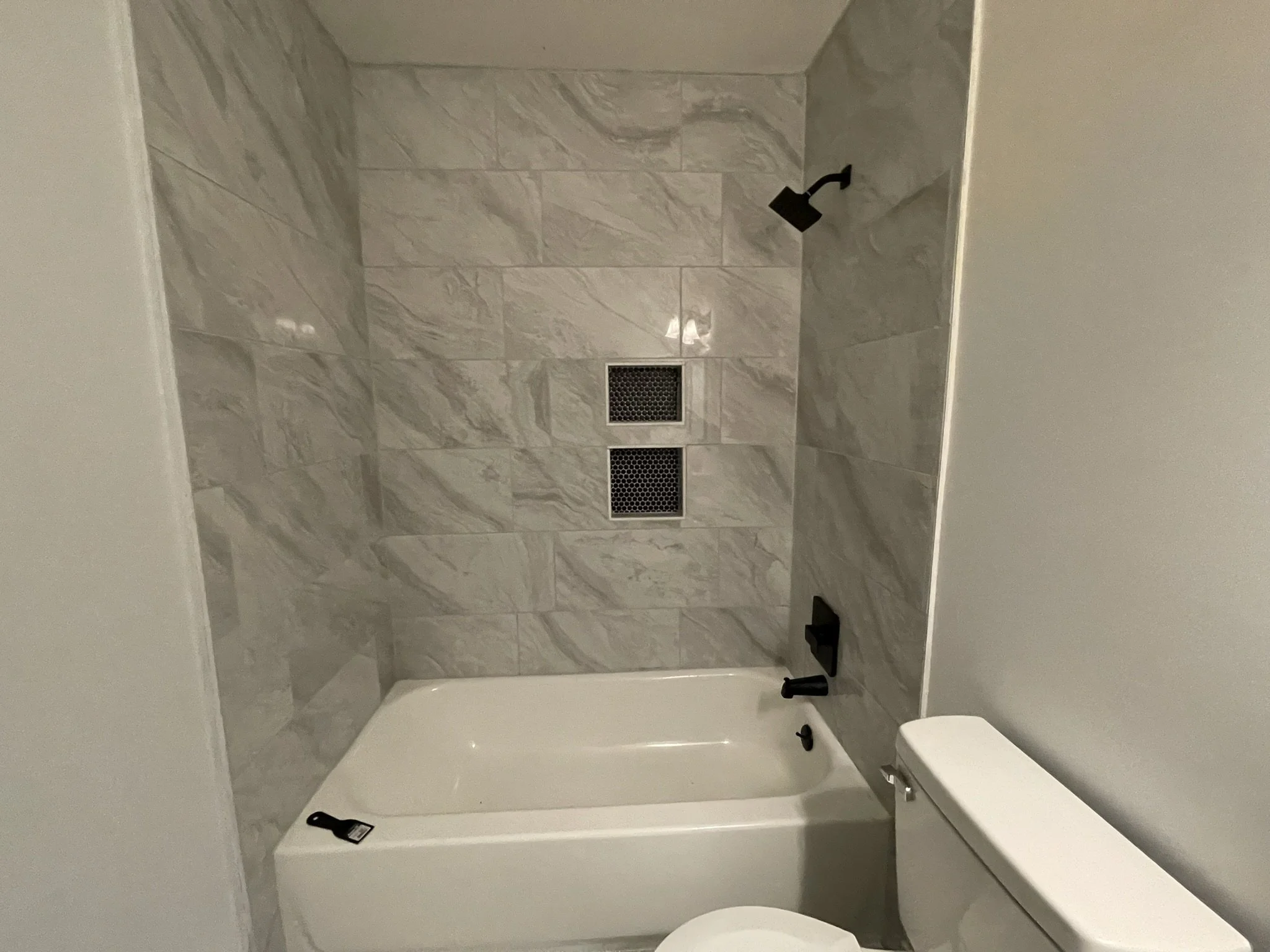 Bathroom with a bathtub, gray marble tiles on the wall, a black showerhead, and a toilet.