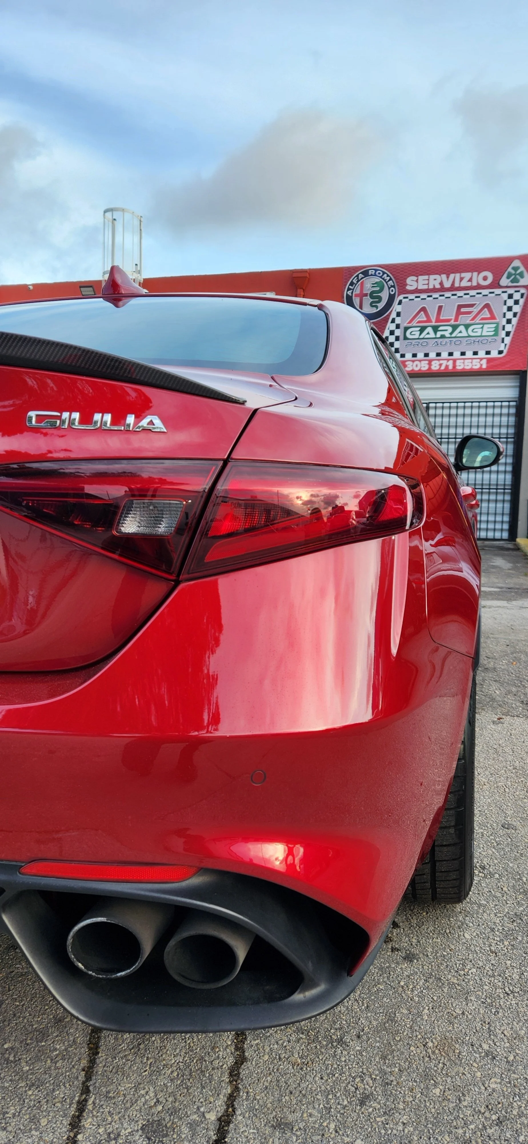 Rear of a red Alfa Romeo Giulia parked at a service garage, with the garage sign in the background.