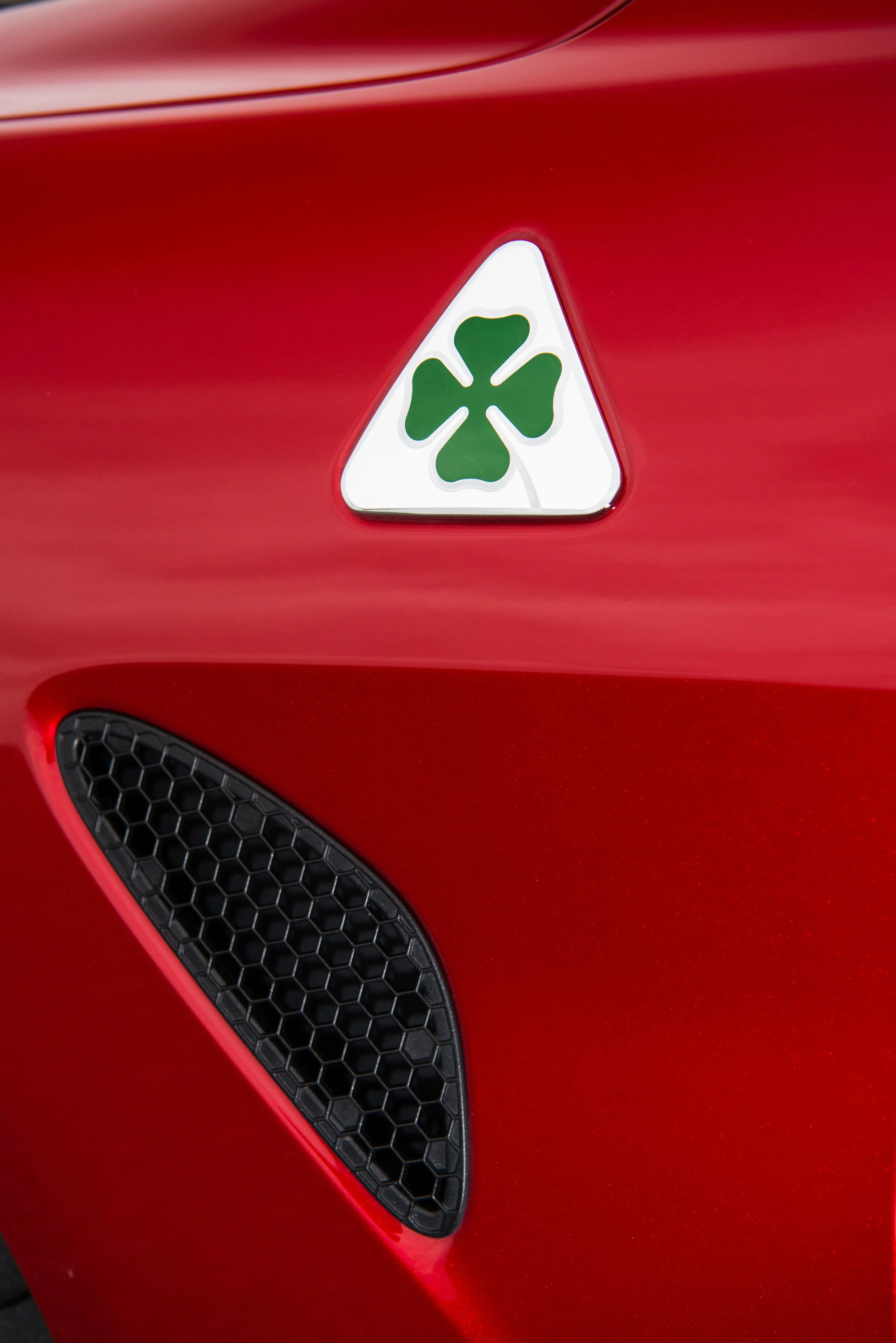 Close-up of a red sports car with a white triangle emblem featuring a green four-leaf clover on the front hood.