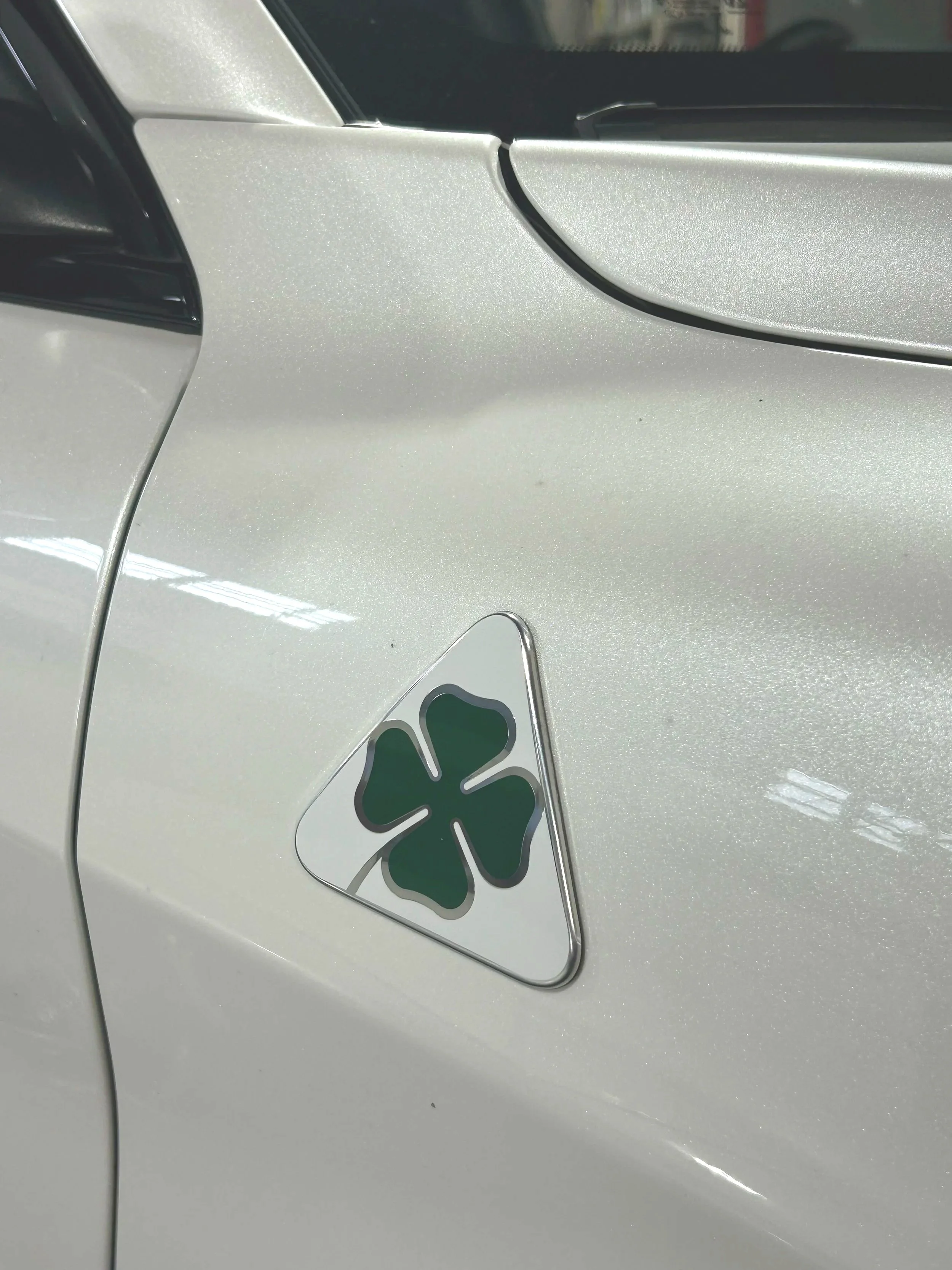 A close-up photo of a metallic silver car with a four-leaf clover-shaped parking permit hanging from the rearview mirror.