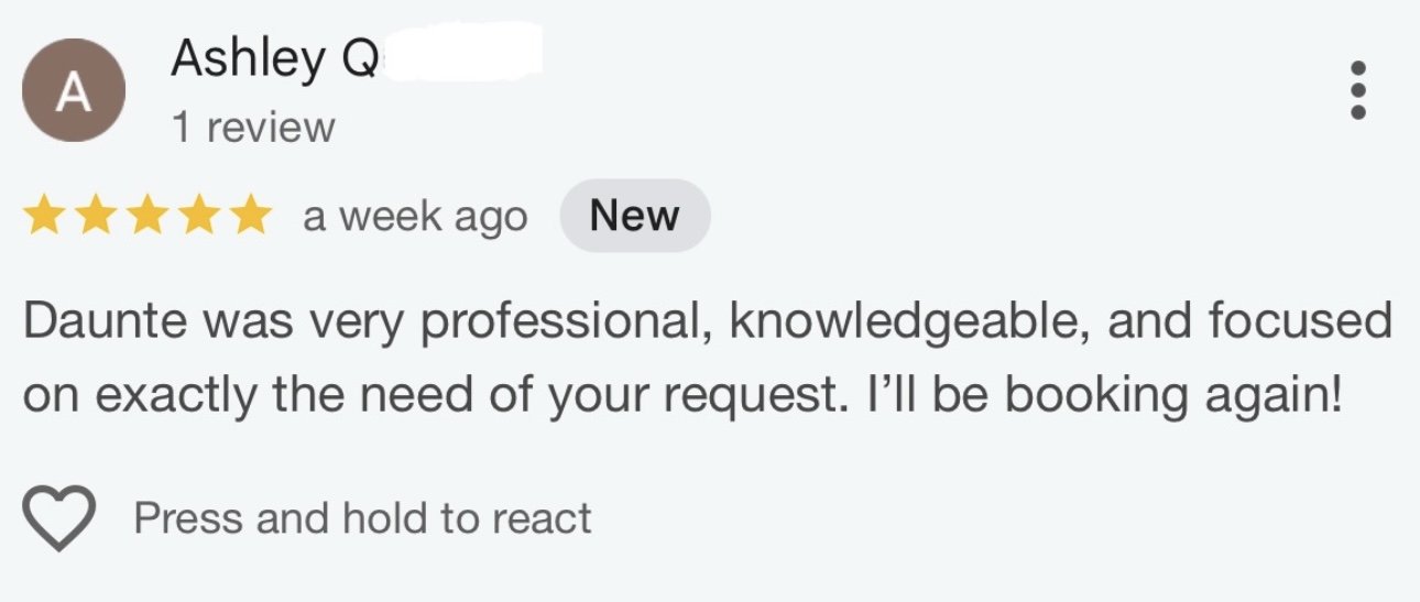 Photo of a large lake with green hills and towering mountains in the background, under an overcast sky.