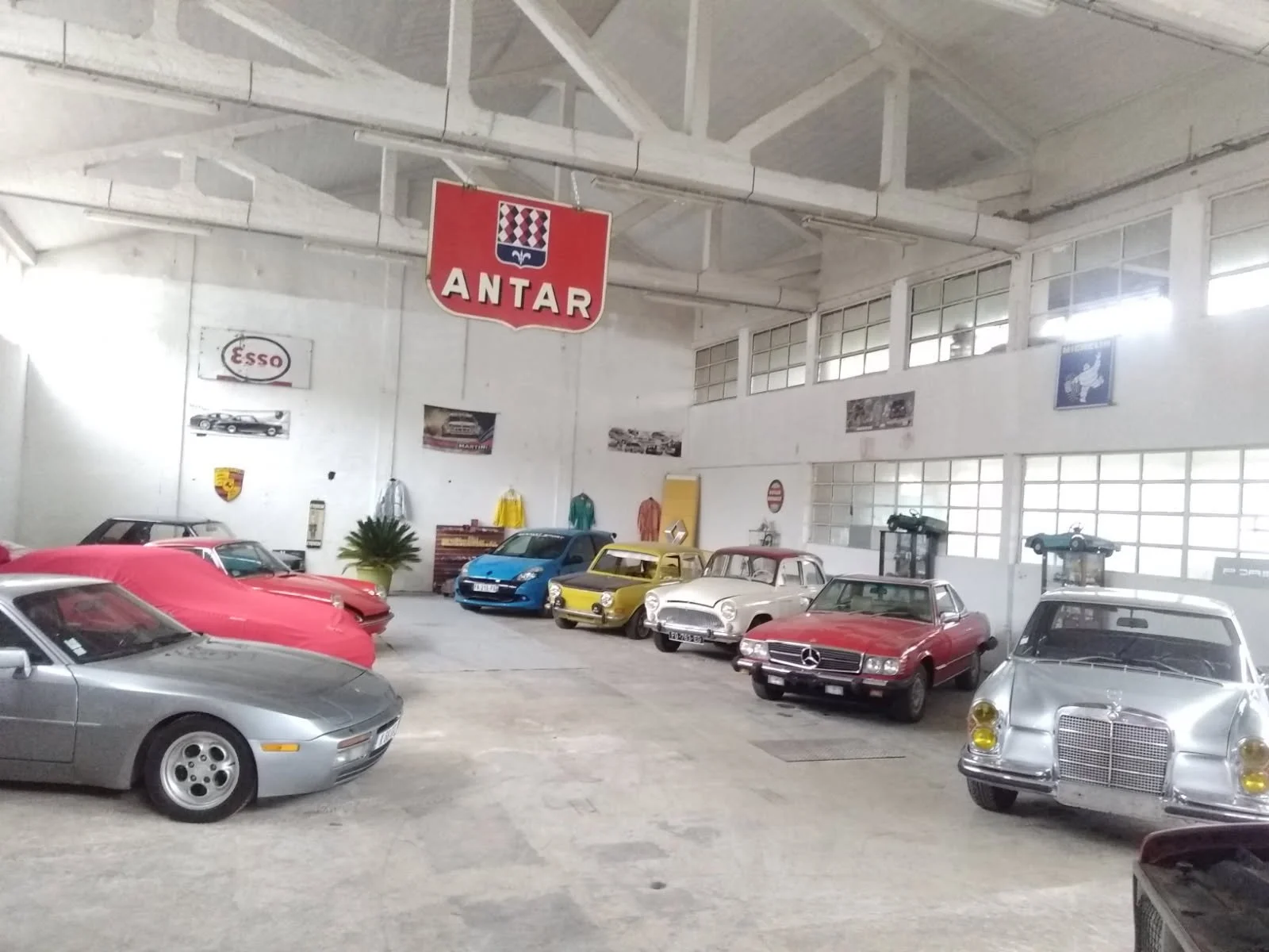 Une collection de voitures anciennes dans un garage avec des plaques, affiches et un panneau avec la carte d'Antar