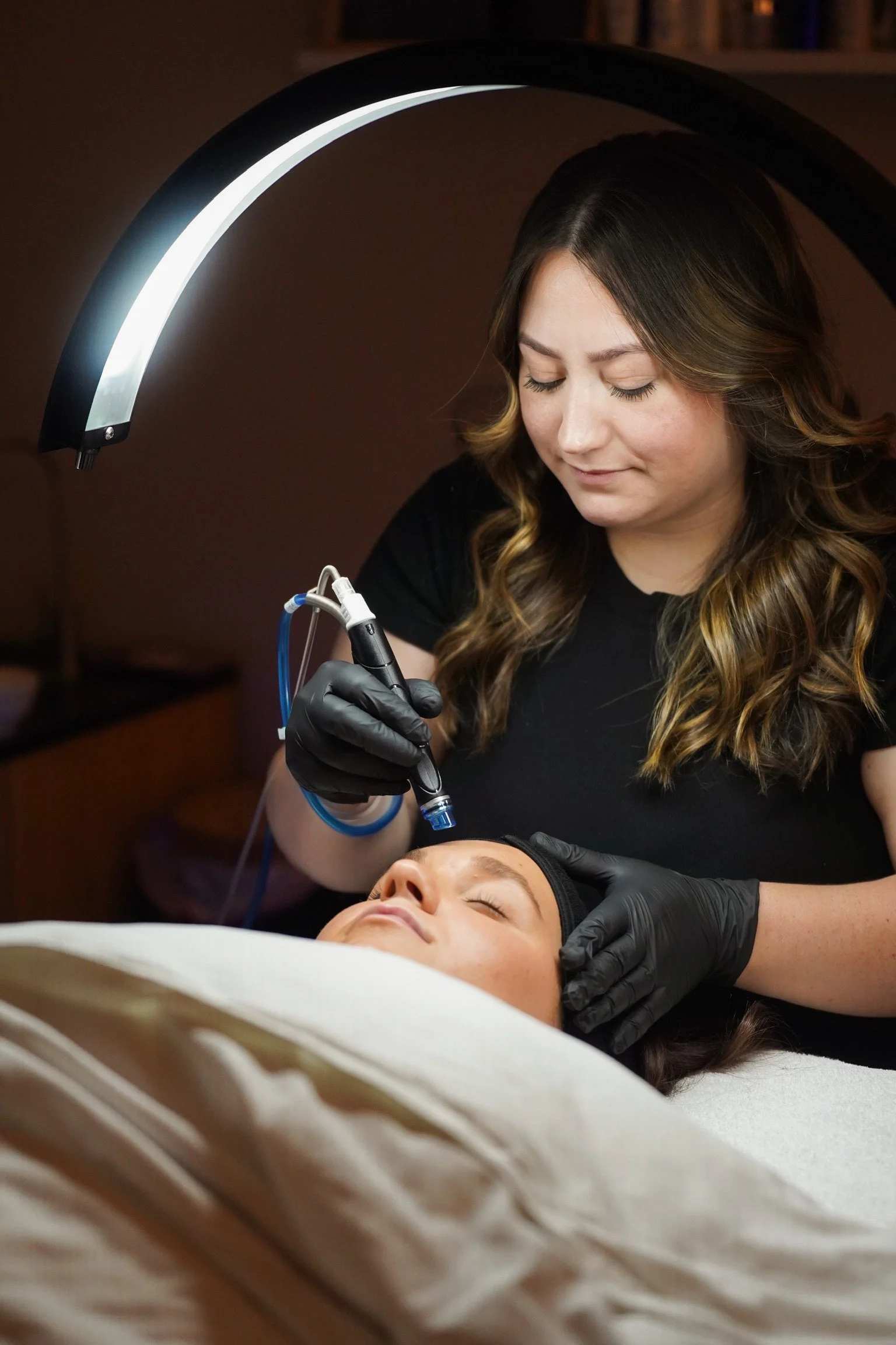 A woman getting a laser or microneedling facial treatment from an aesthetician in a spa or clinic setting.