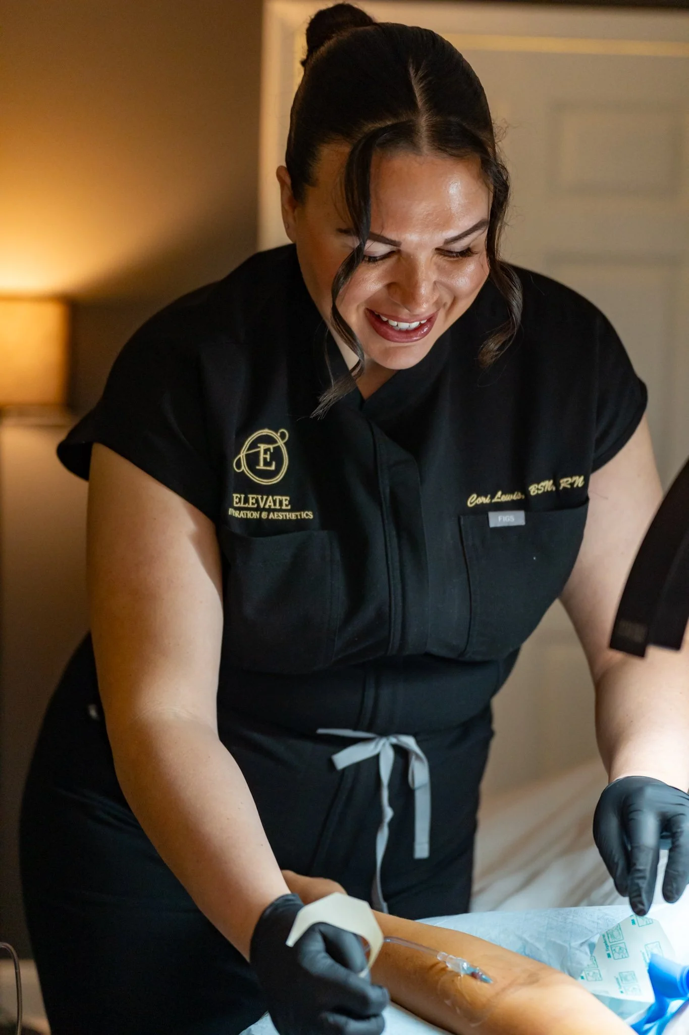 A healthcare professional wearing black gloves administers an injection into a patient's leg using a syringe and a cotton ball for pressure.
