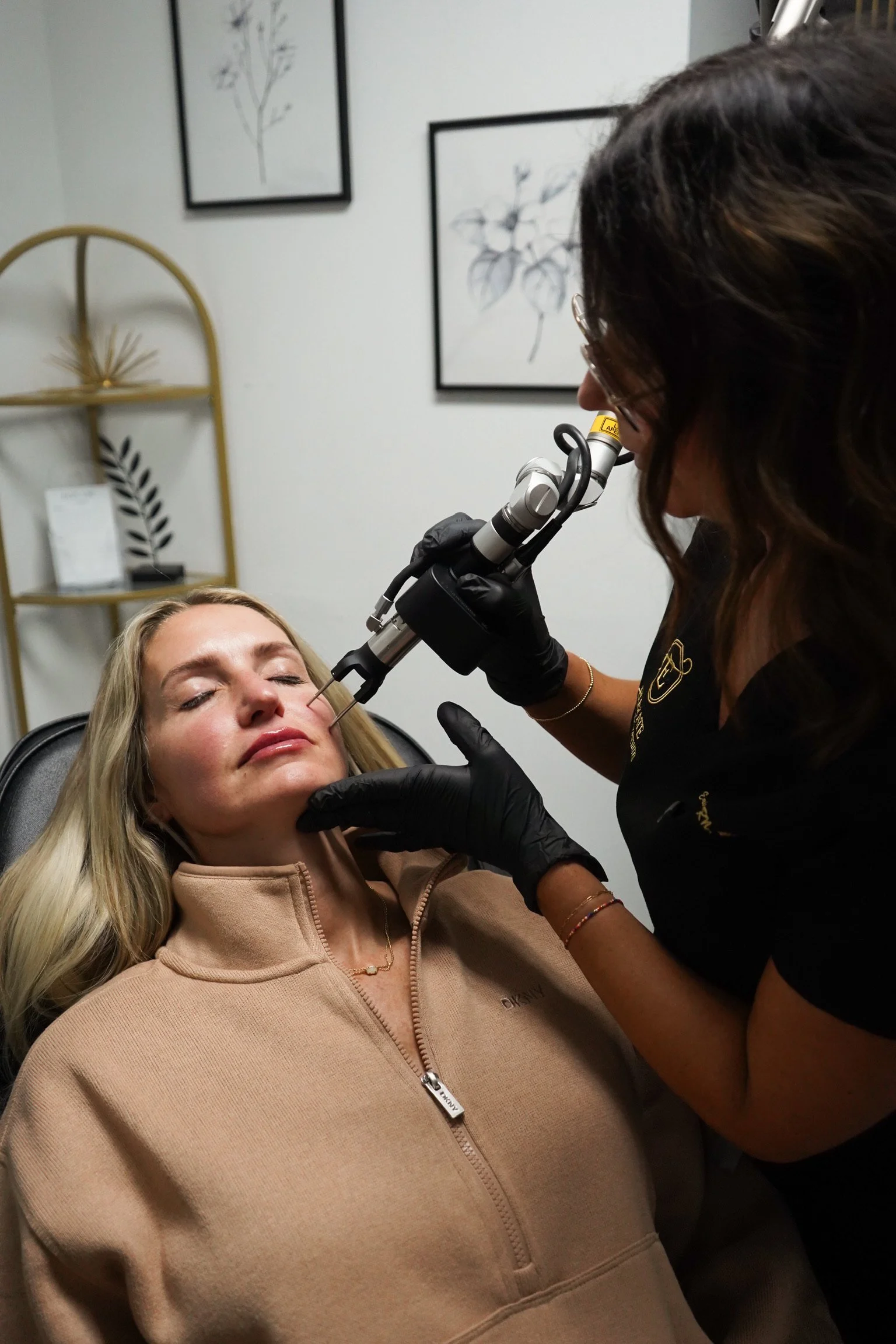 A person receiving a cosmetic procedure on their face from a professional using a specialized medical tool in a clinic room.