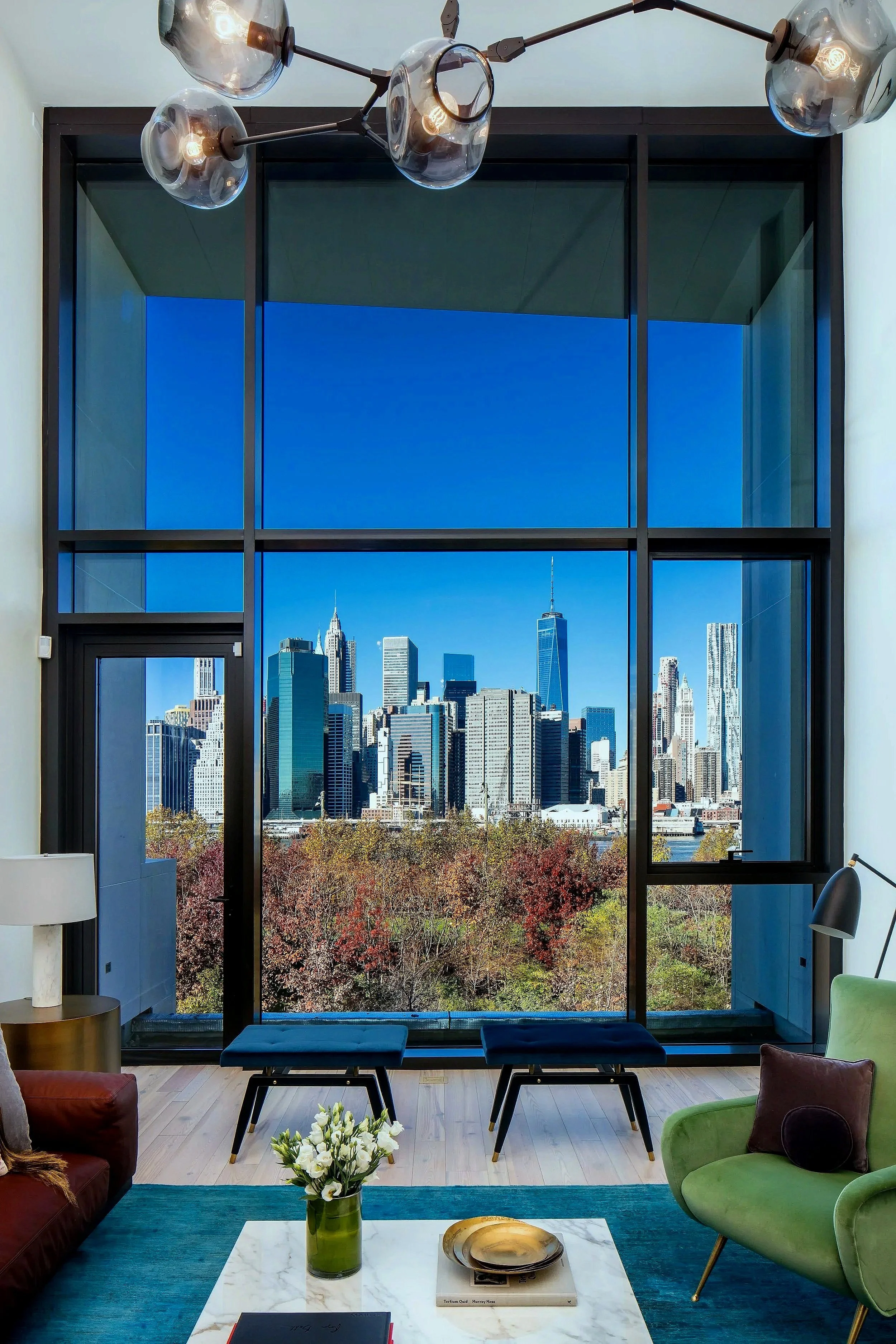 View of New York City skyline through large floor-to-ceiling window in a modern living room.