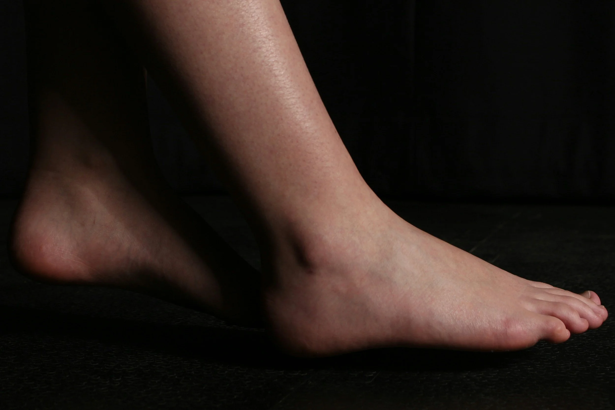 A close-up of a person's bare feet on a dark surface against a dark background.