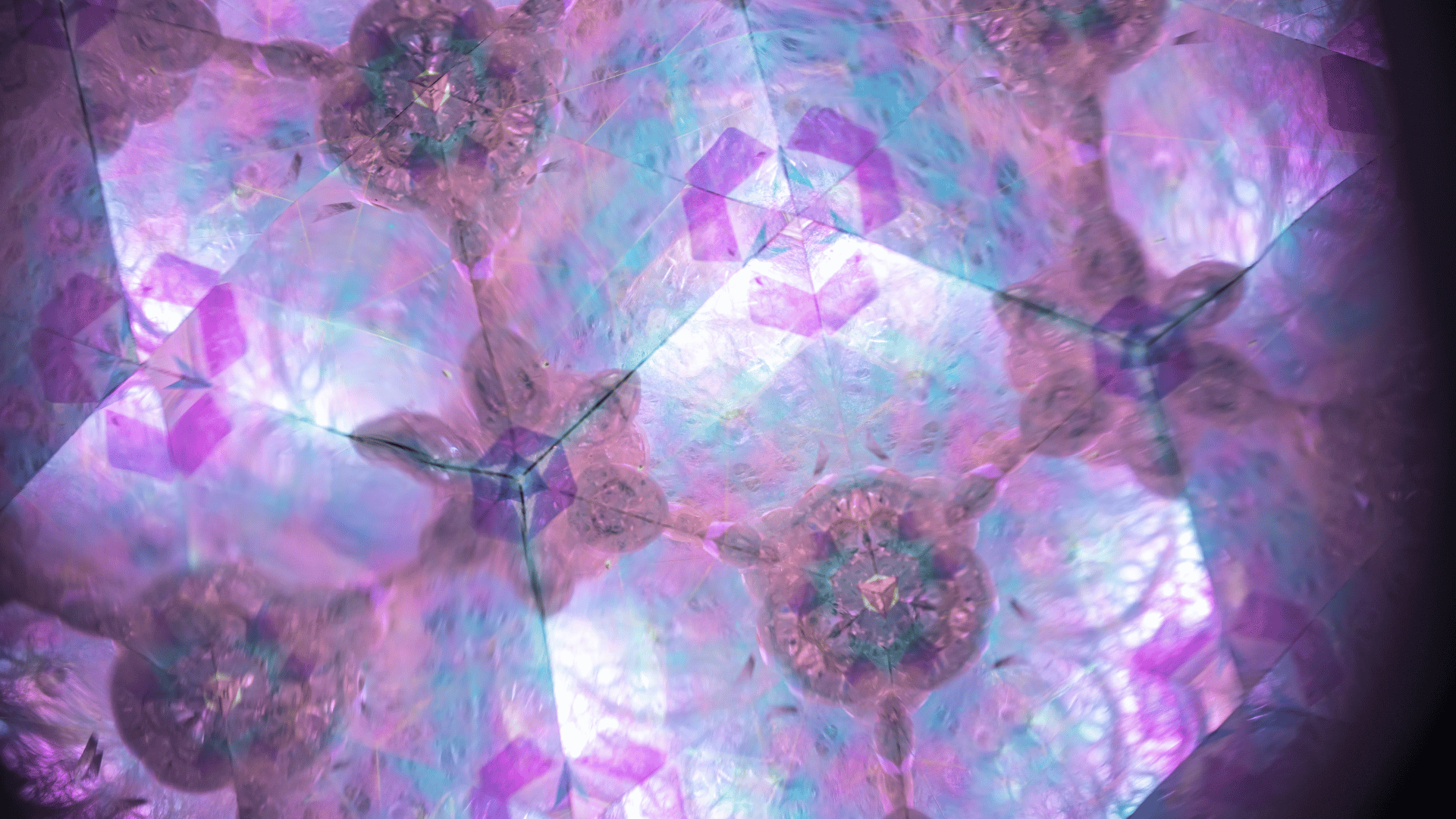 A close-up of a colorful, iridescent, and reflective crystal or glass art piece illuminated with shades of pink, purple, and blue.