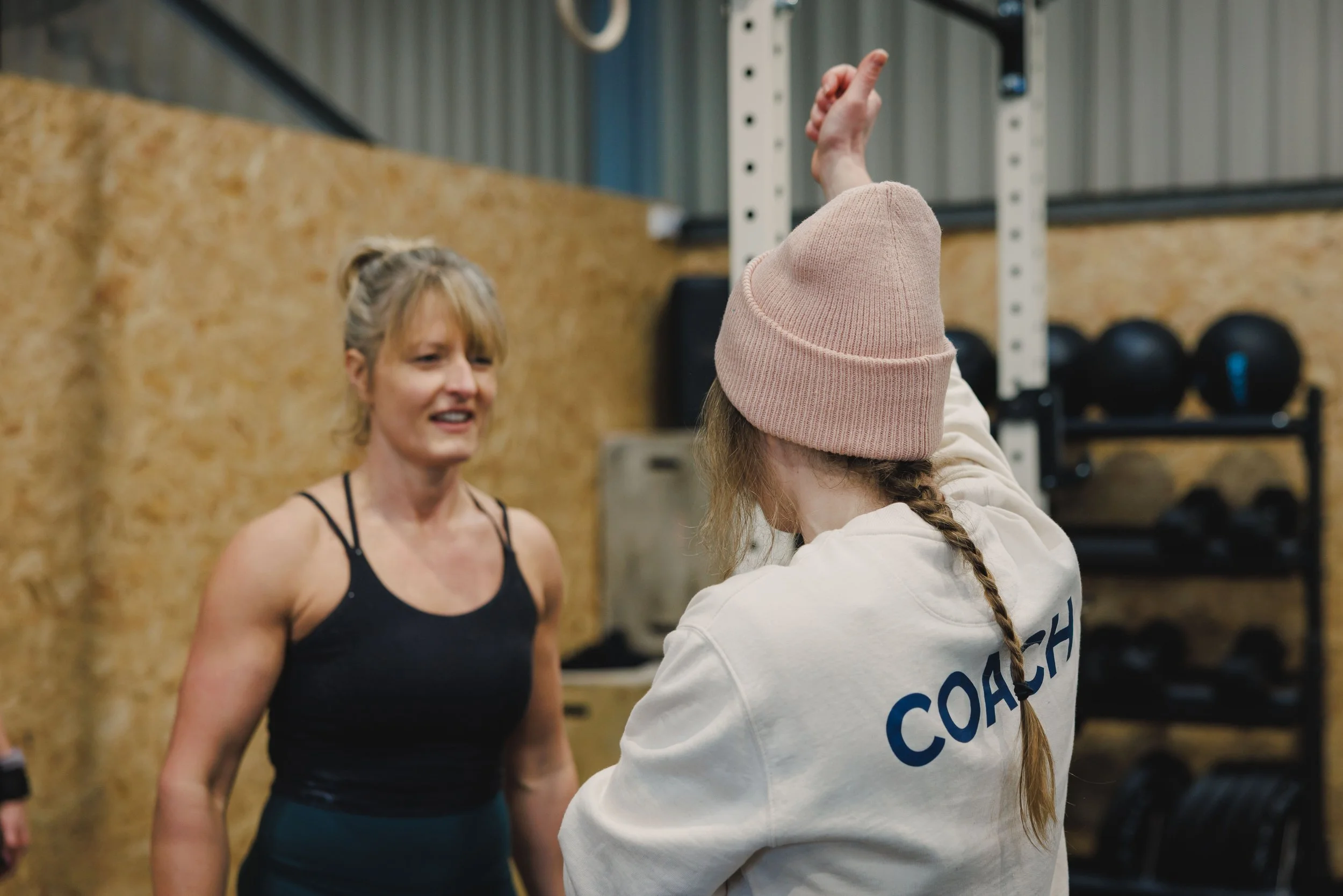 A woman talking to a coach in a gym with weight racks in the background.