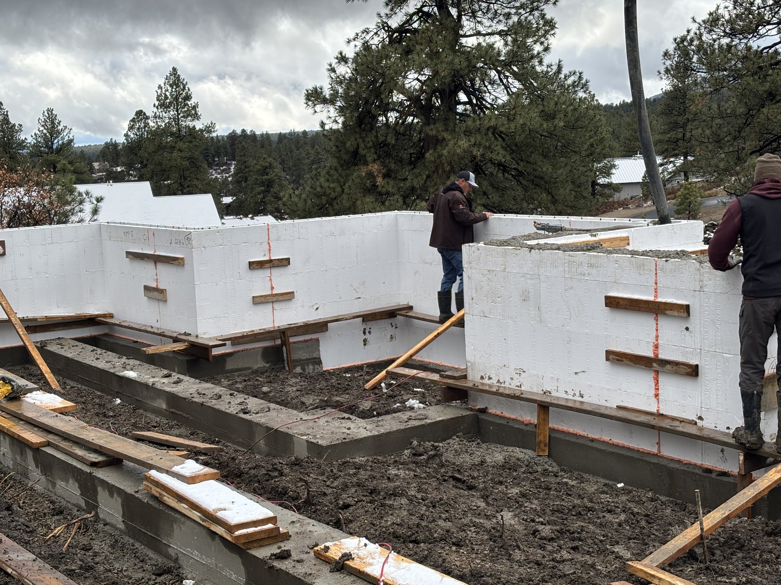 Construction site with workers building a foundation using large blocks of expanded polystyrene insulation material for a building.