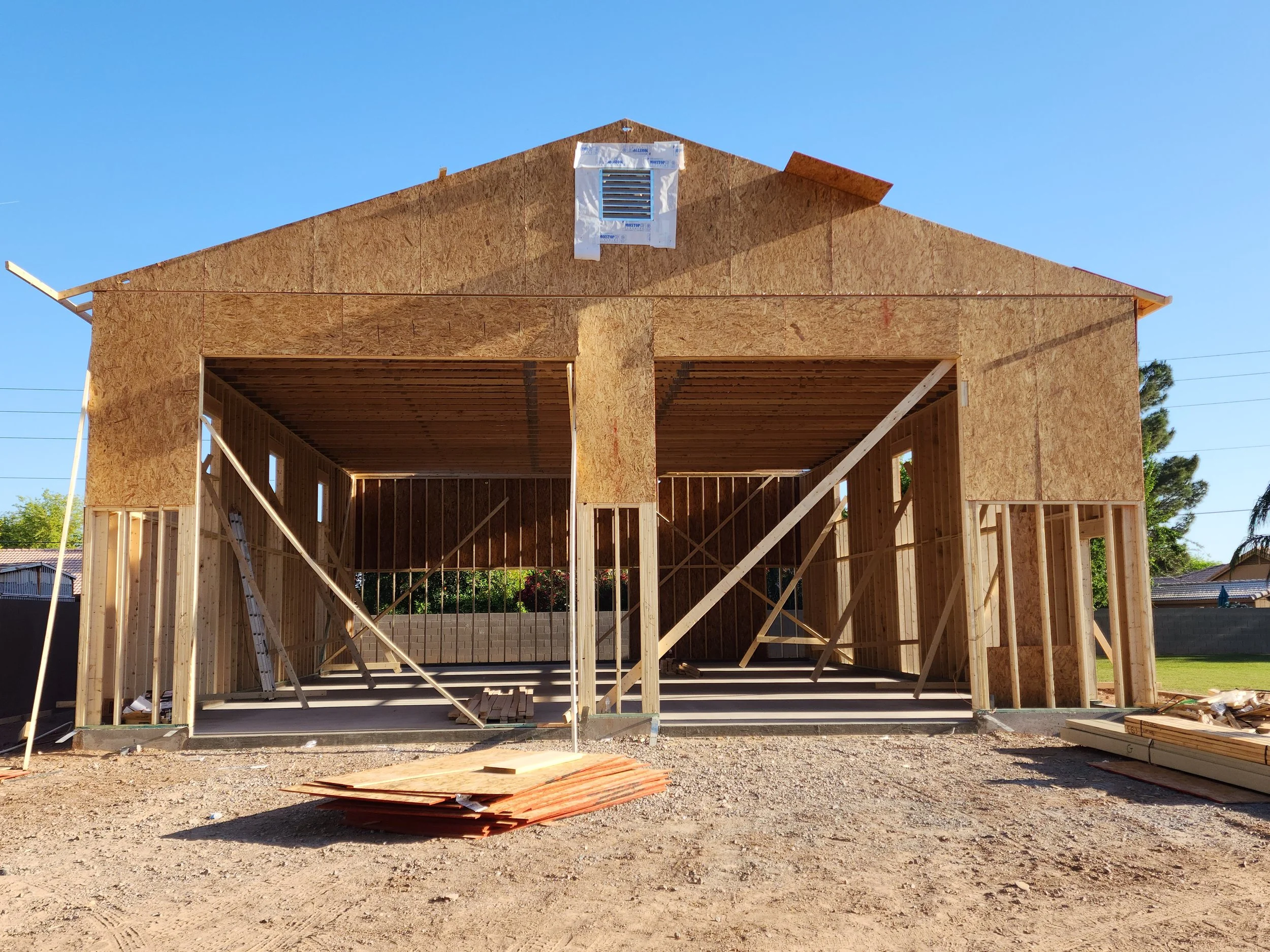 The frame of a house under construction, with plywood panels and wooden beams, in a clear outdoor setting.
