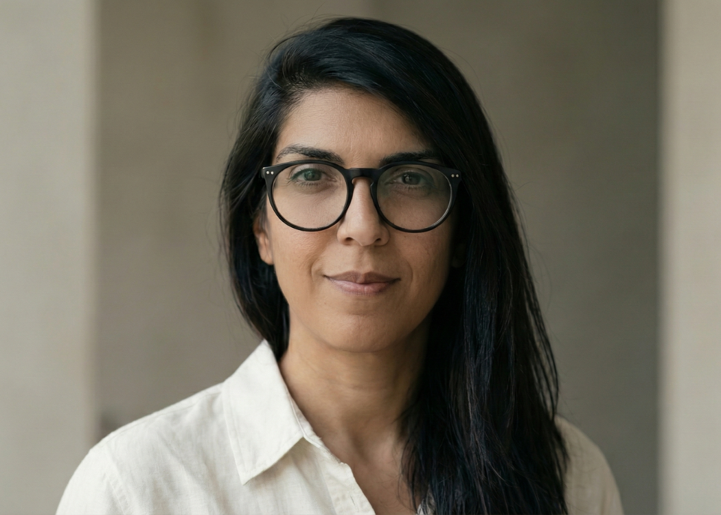 Portrait of a woman with black hair, wearing black-rimmed glasses and a white shirt, smiling softly.
