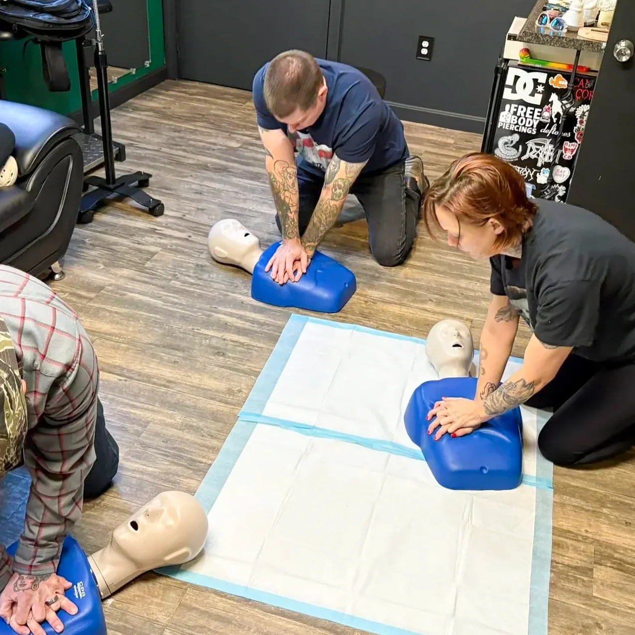 Two people practicing hands-only CPR on mannequin dummies in a training class.