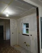 A room under renovation with unfinished walls, a small window, and construction materials on the floor.