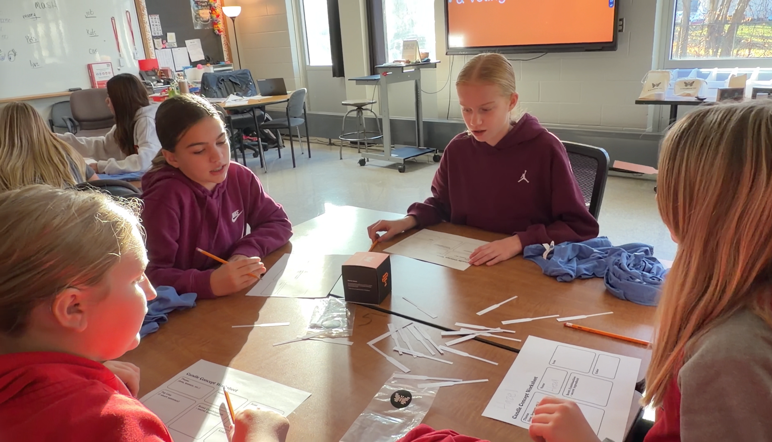 Five children sitting around a table in a classroom, working on a project with paper, straws, and pencils.