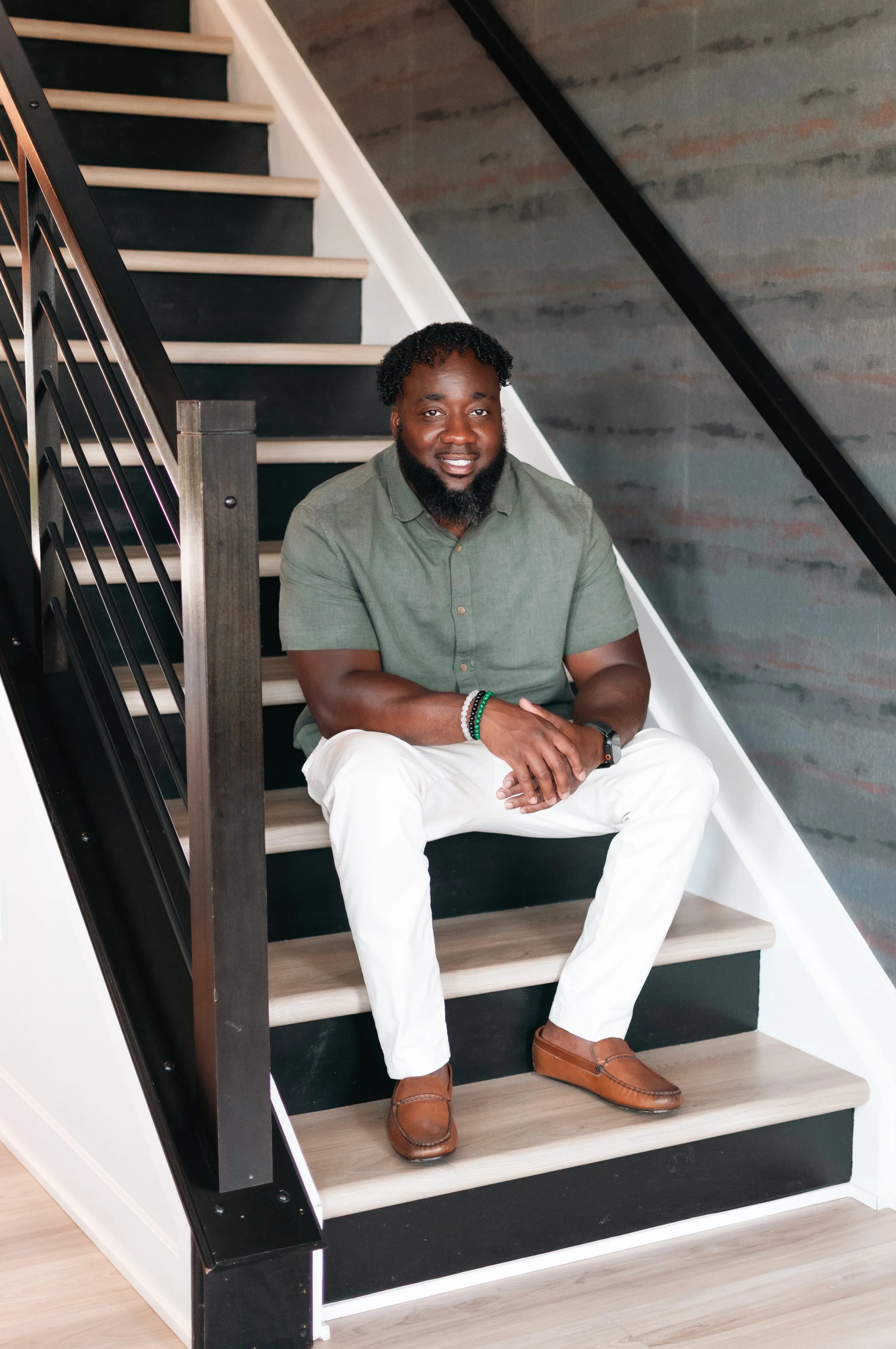 A man sitting on a staircase with a modern industrial design, smiling at the camera.