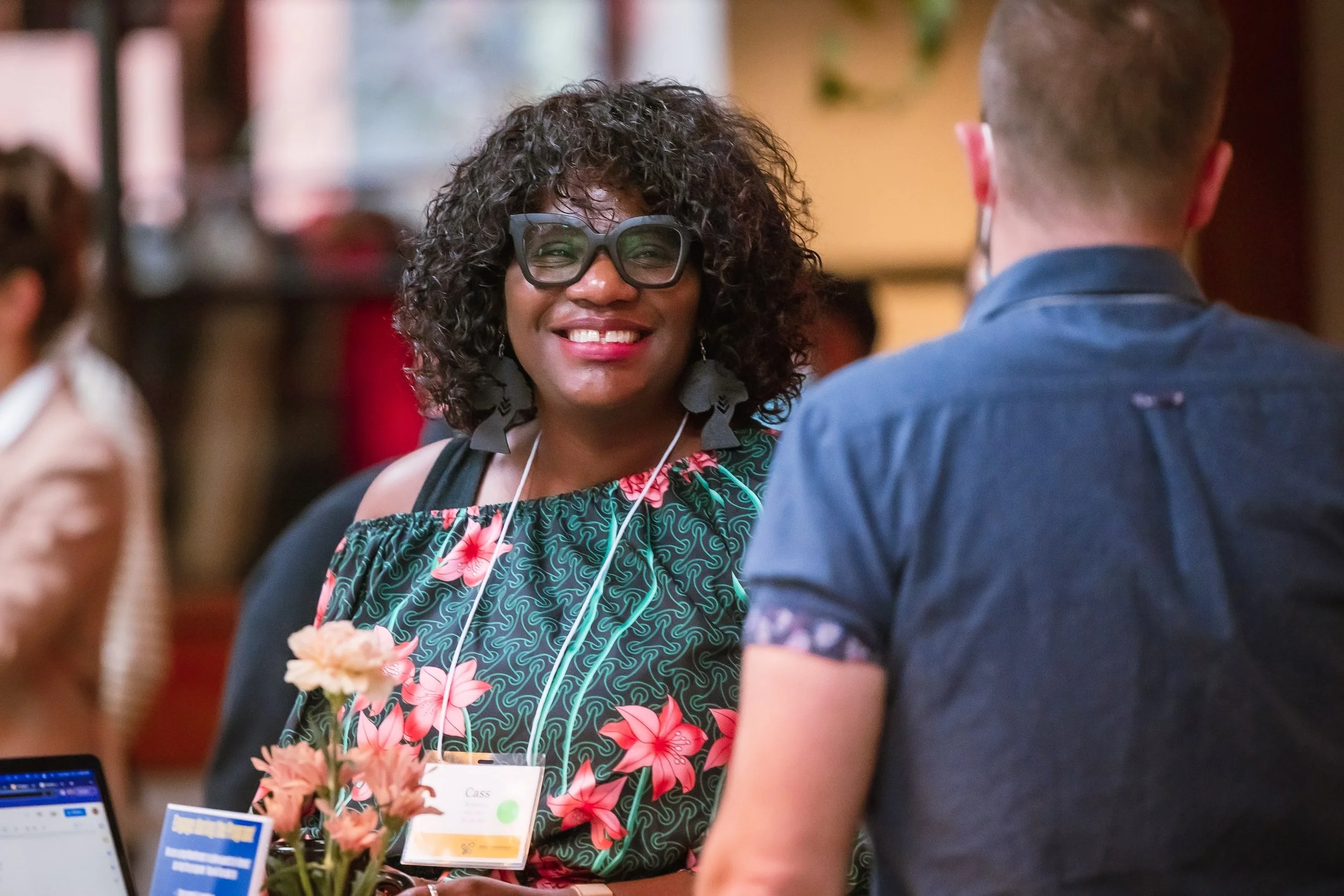 A woman with curly hair, glasses, and large earrings smiling at a man with short hair at a social event.