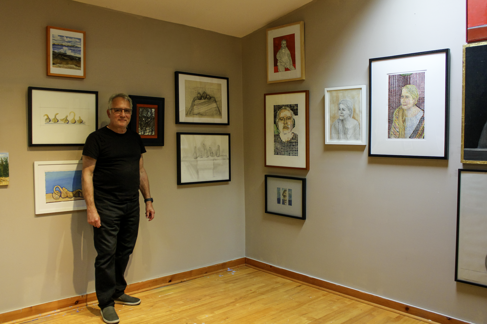 Dean Vallas standing in an art gallery with various framed artwork and photographs on the wall behind him.