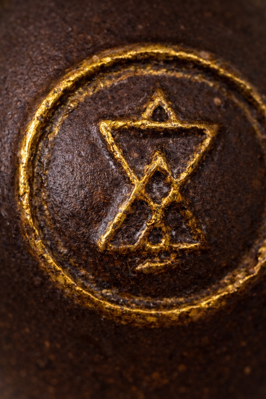 Un symbole en or gravé sur une surface en métal rouillée, représentant une étoile à six branches avec une ligne traversante et un autre symbole au centre.
