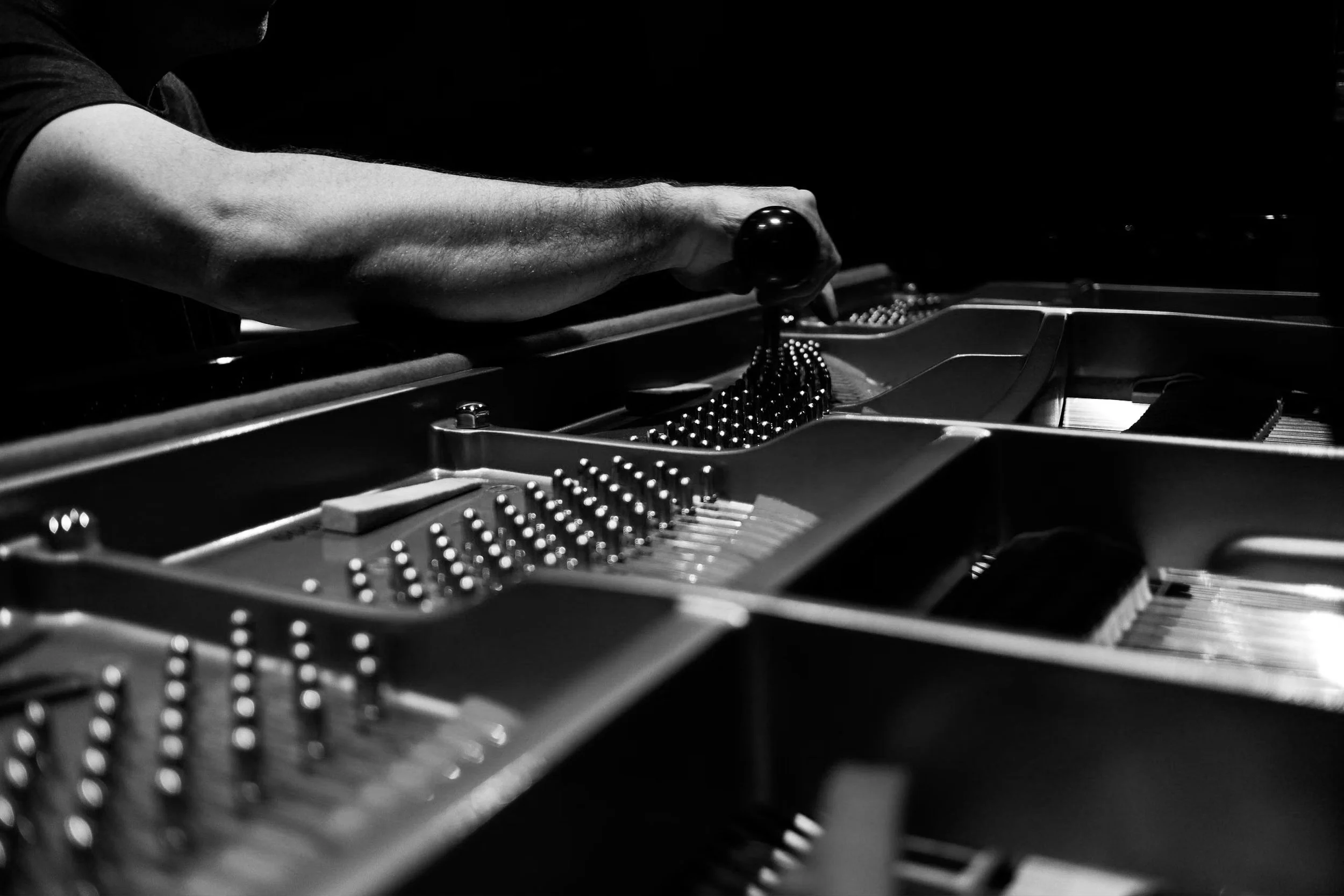 Black and white photo of a person playing a grand piano, focusing on their arm and hand pressing the piano keys.