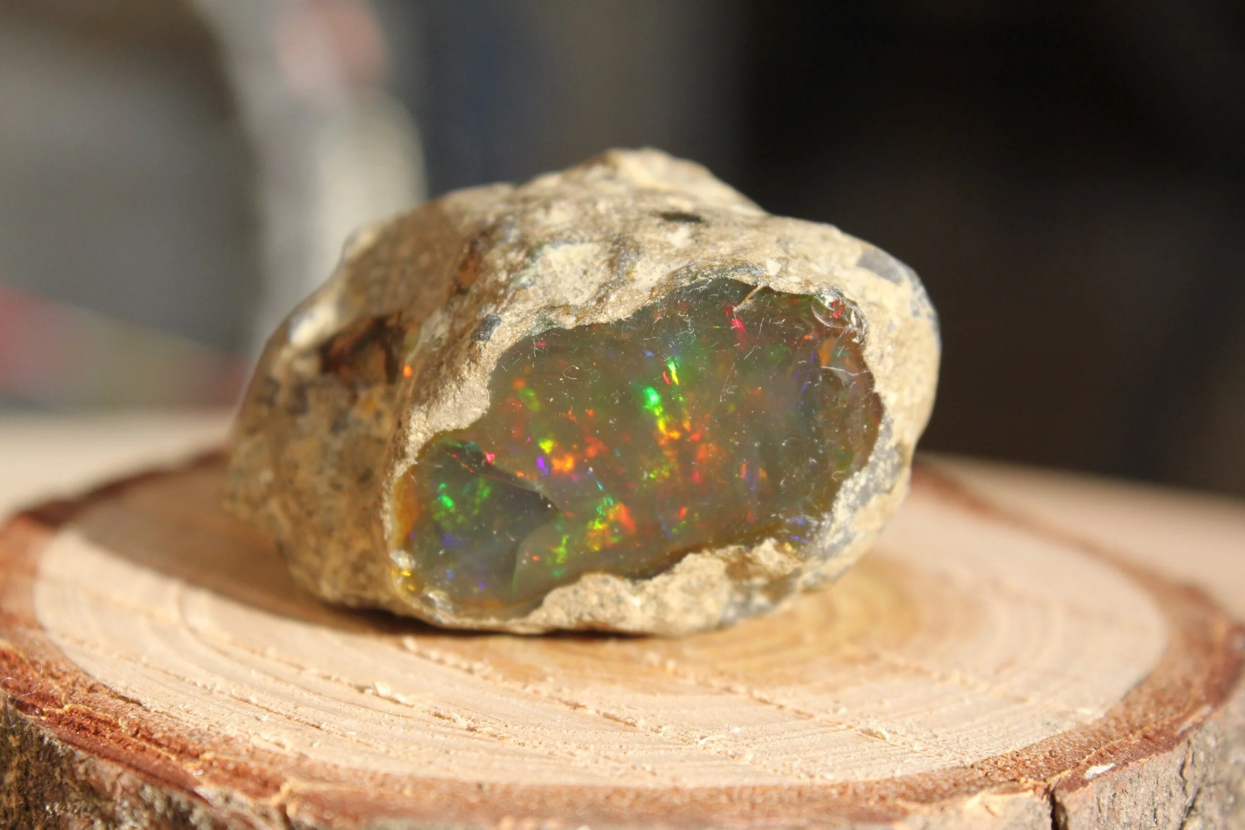 Gros plan sur une pierre contenant un fragment d'opale avec des reflets colorés, posé sur une tranche de bois.