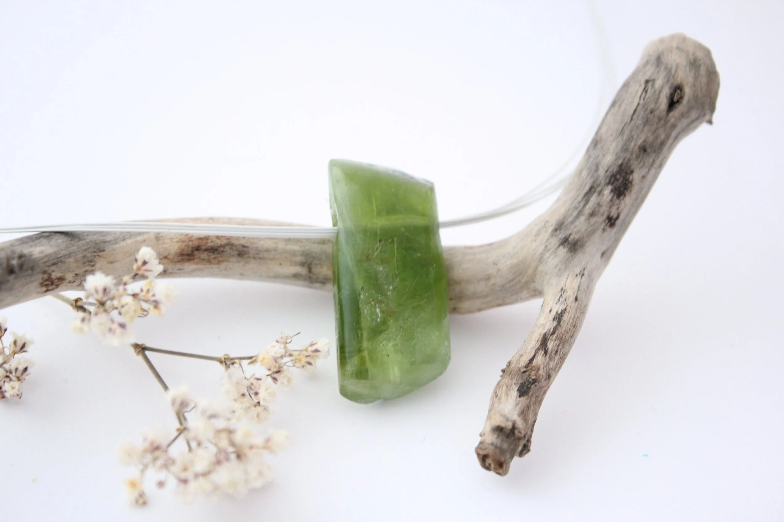 Une pierre verte posée sur un morceau de bois flotté avec des fleurs blanches petites