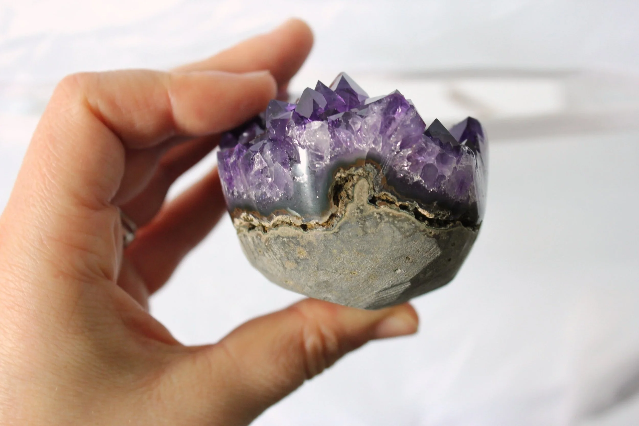 Main tenant un géode de quartz violet, moitié ouverte, montrant des cristaux violets à l'intérieur.