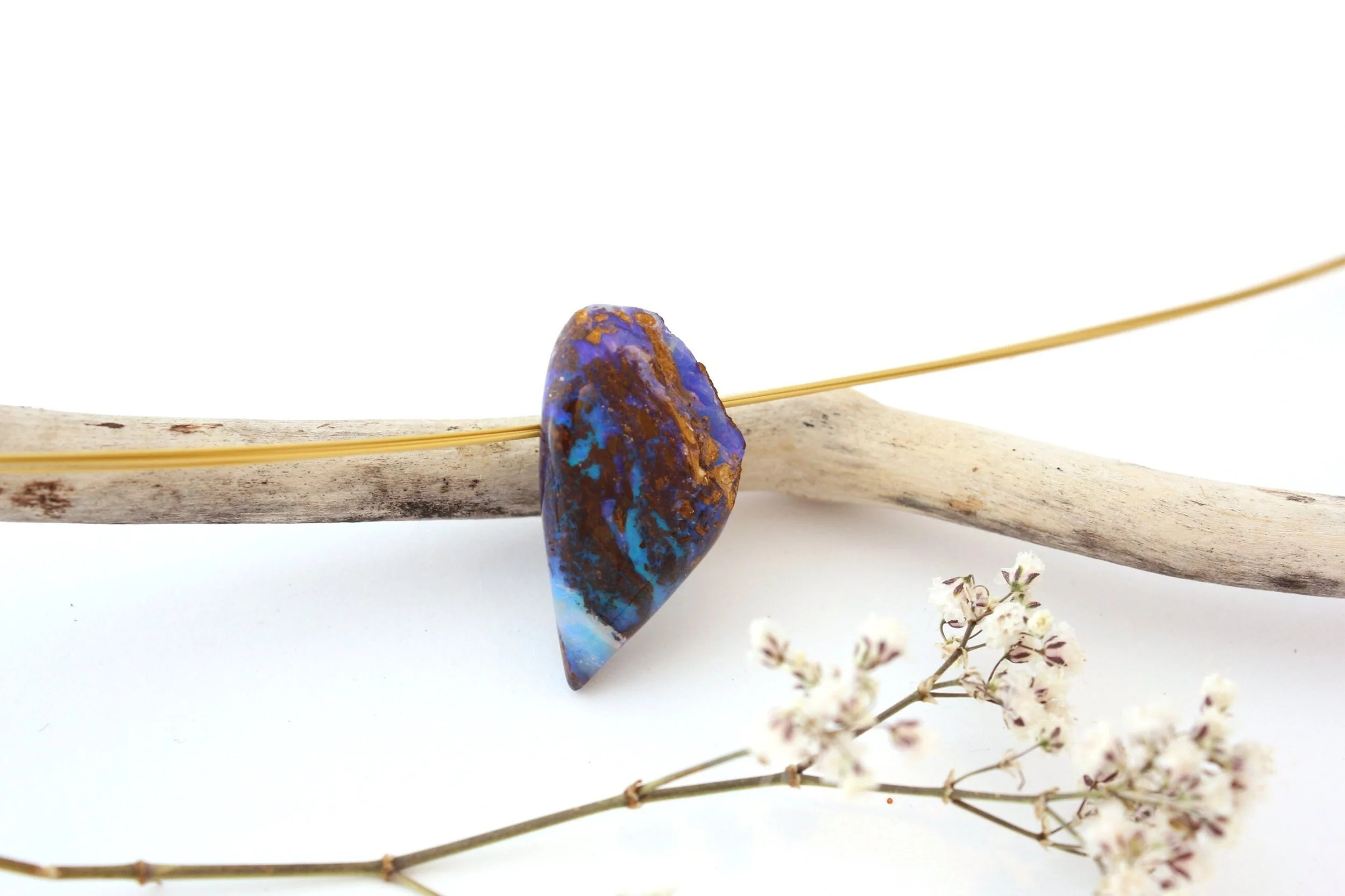 Une pierre bleue et marron en forme d'aileron, posée sur un bâton en bois avec une branche de fleurs blanches en dessous.