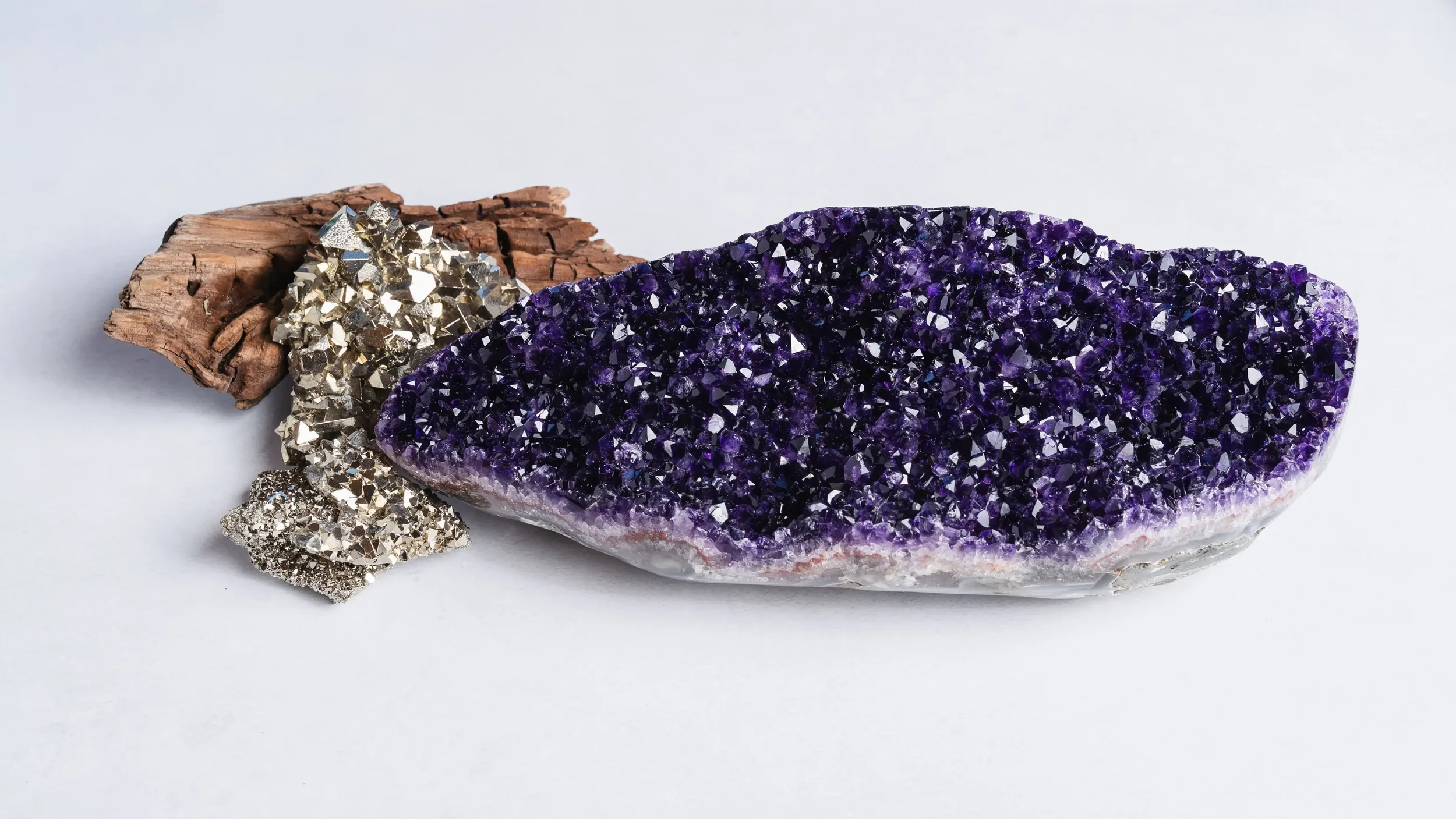 Gisements de minéraux et cristaux violets, en particulier une grande plaque d'améthyste, avec des morceaux d'autre minéraux argentés et une pièce de bois en arrière-plan.
