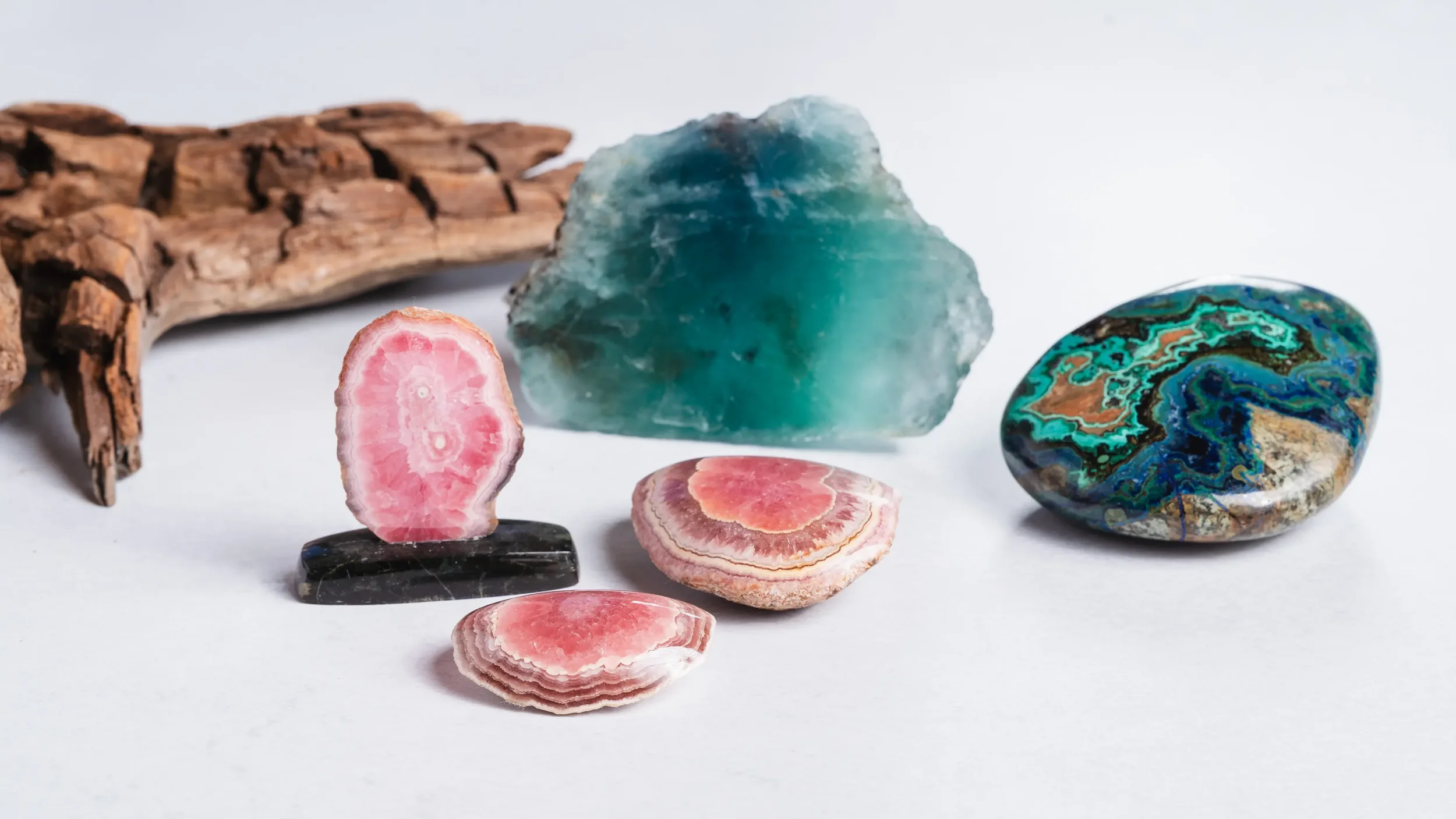 Groupe de pierres semi-précieuses colorées et d'une branche de bois rustique sur fond blanc.