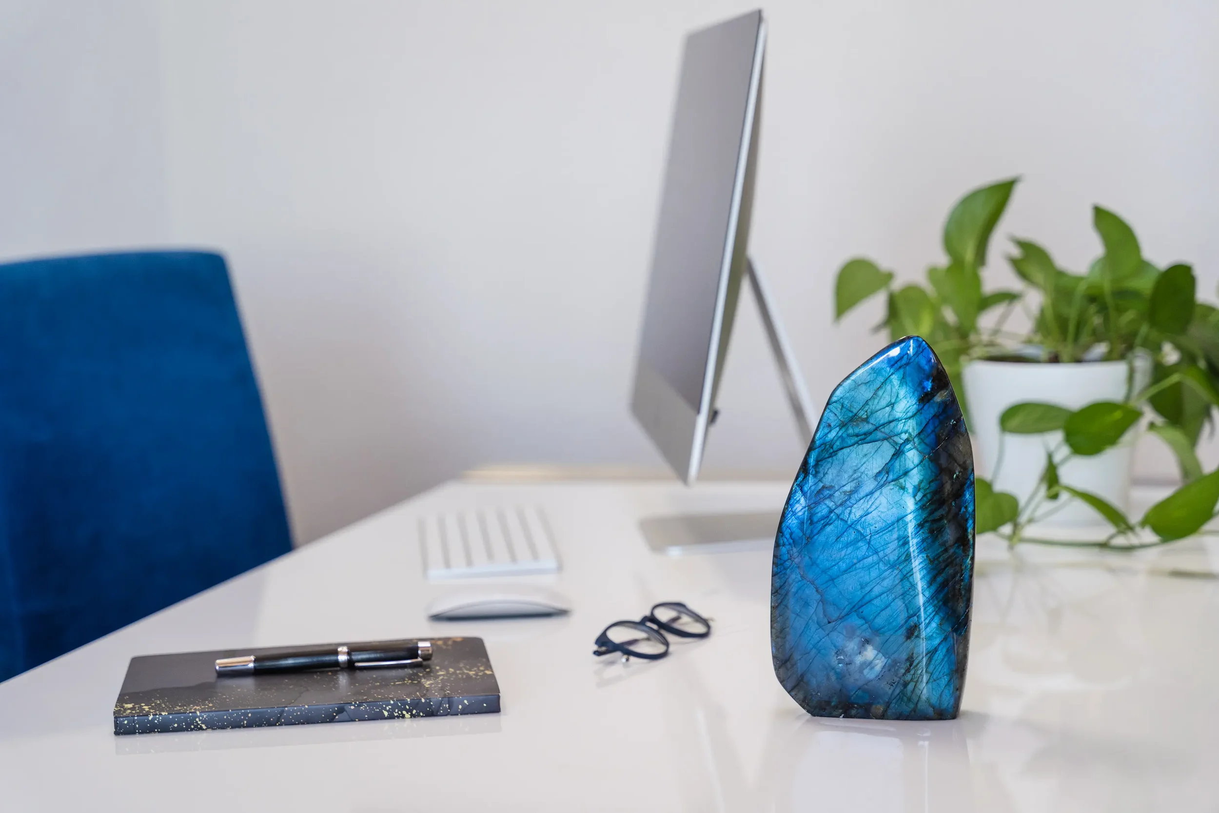 Un bureau moderne avec un ordinateur, une plante verte en pot, des lunettes, un stylo sur un carnet et une sculpture en pierre bleue