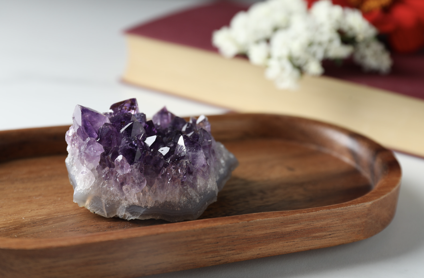 Gisement d'améthystes violettes placé dans un plateau en bois, avec un livre et des fleurs à l'arrière-plan