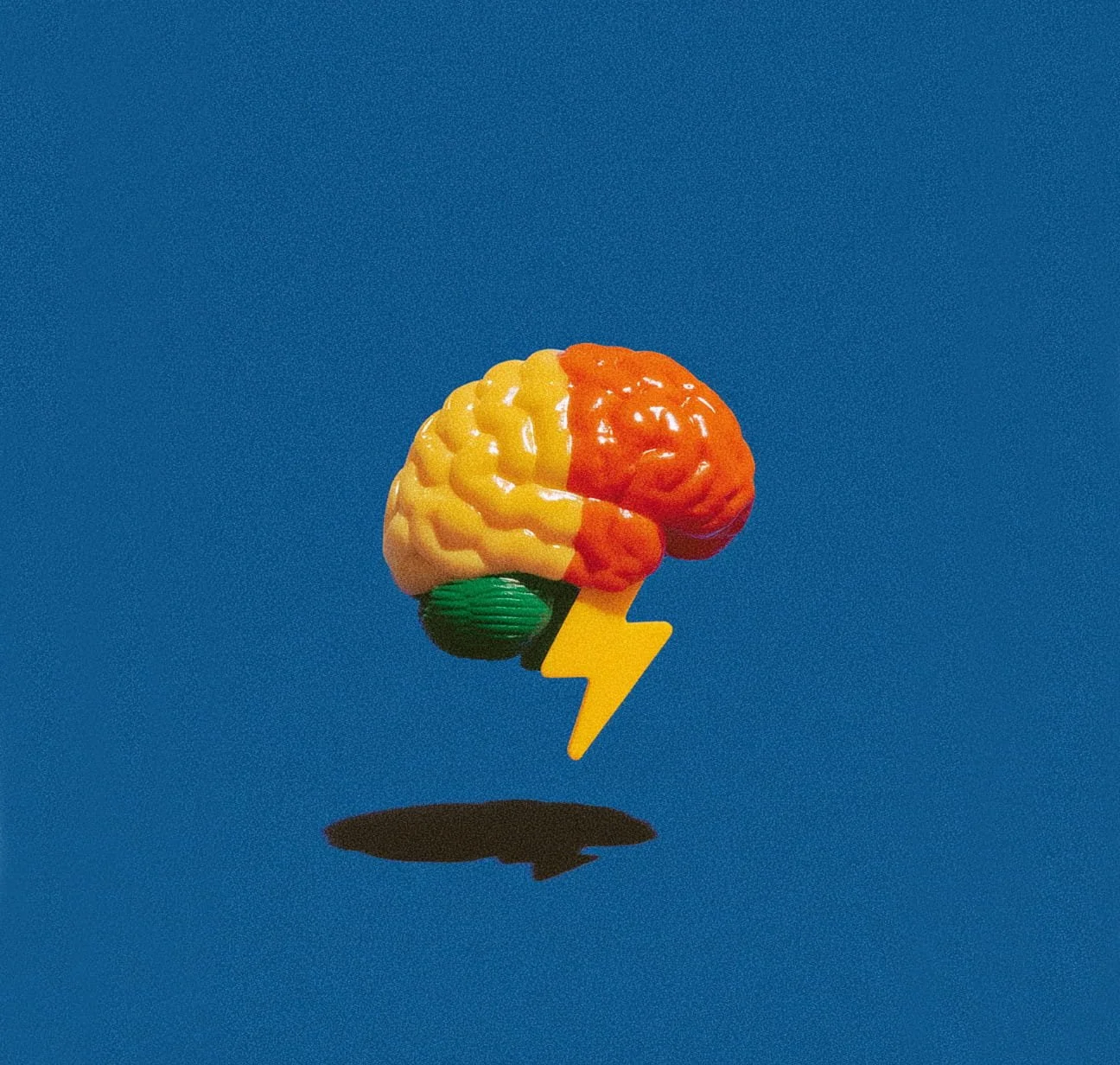 A colorful toy in the shape of a brain with yellow, red, and green sections, featuring a yellow lightning bolt attached, against a blue background.