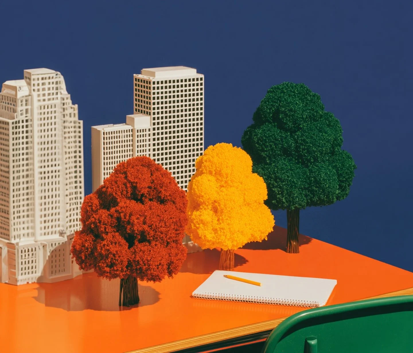 Miniature cityscape with model buildings and colorful paper trees on an orange surface.