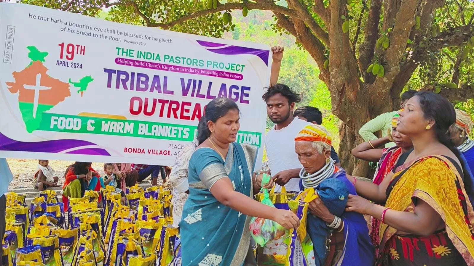 Community members in traditional clothing distributing food and blankets at a tribal village outreach event organized by the India Pastors Project in Bonda village, India, April 19, 2024, under the theme of helping build Christ's kingdom.