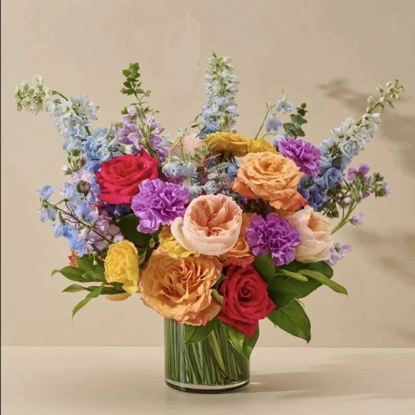 A colorful bouquet of roses, lisianthus, and other flowers in a glass vase.
