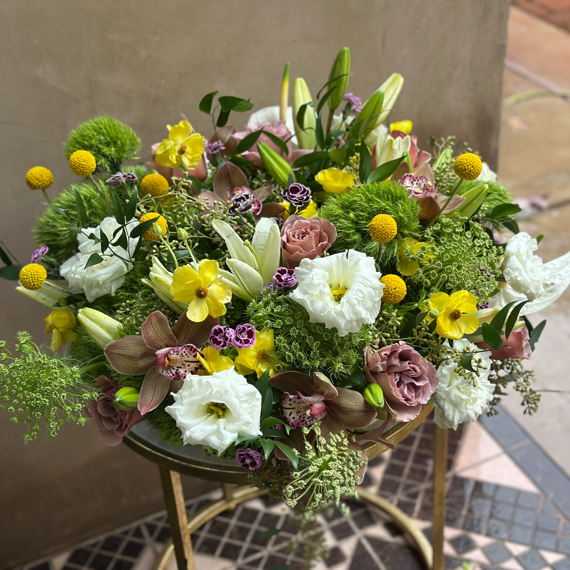 A colorful bouquet of various flowers, including white, yellow, pink, purple, and green blooms, arranged on a gold stand.