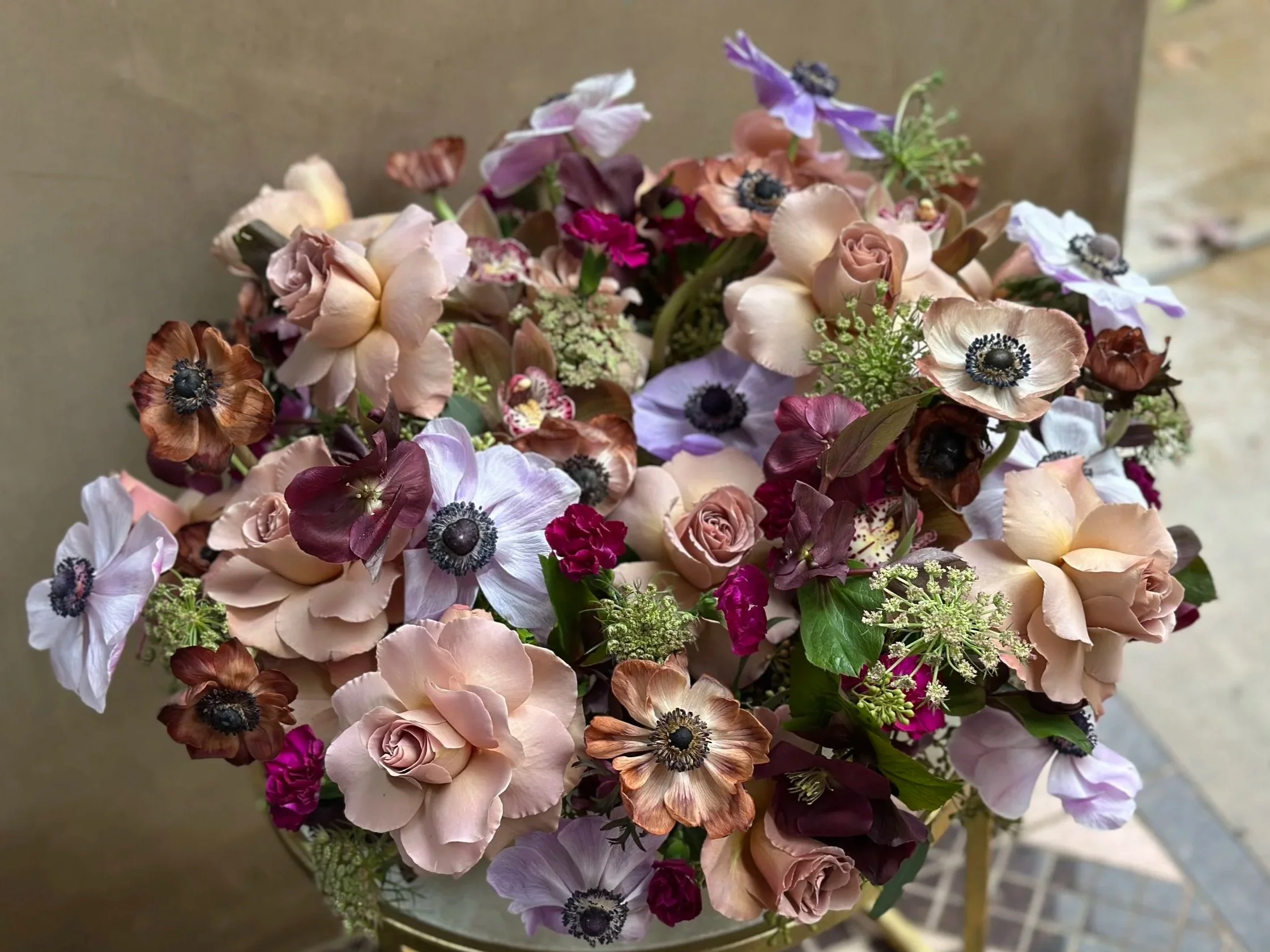 A bouquet of mixed flowers including roses, anemones, and other blossoms in pastel and deep colors.