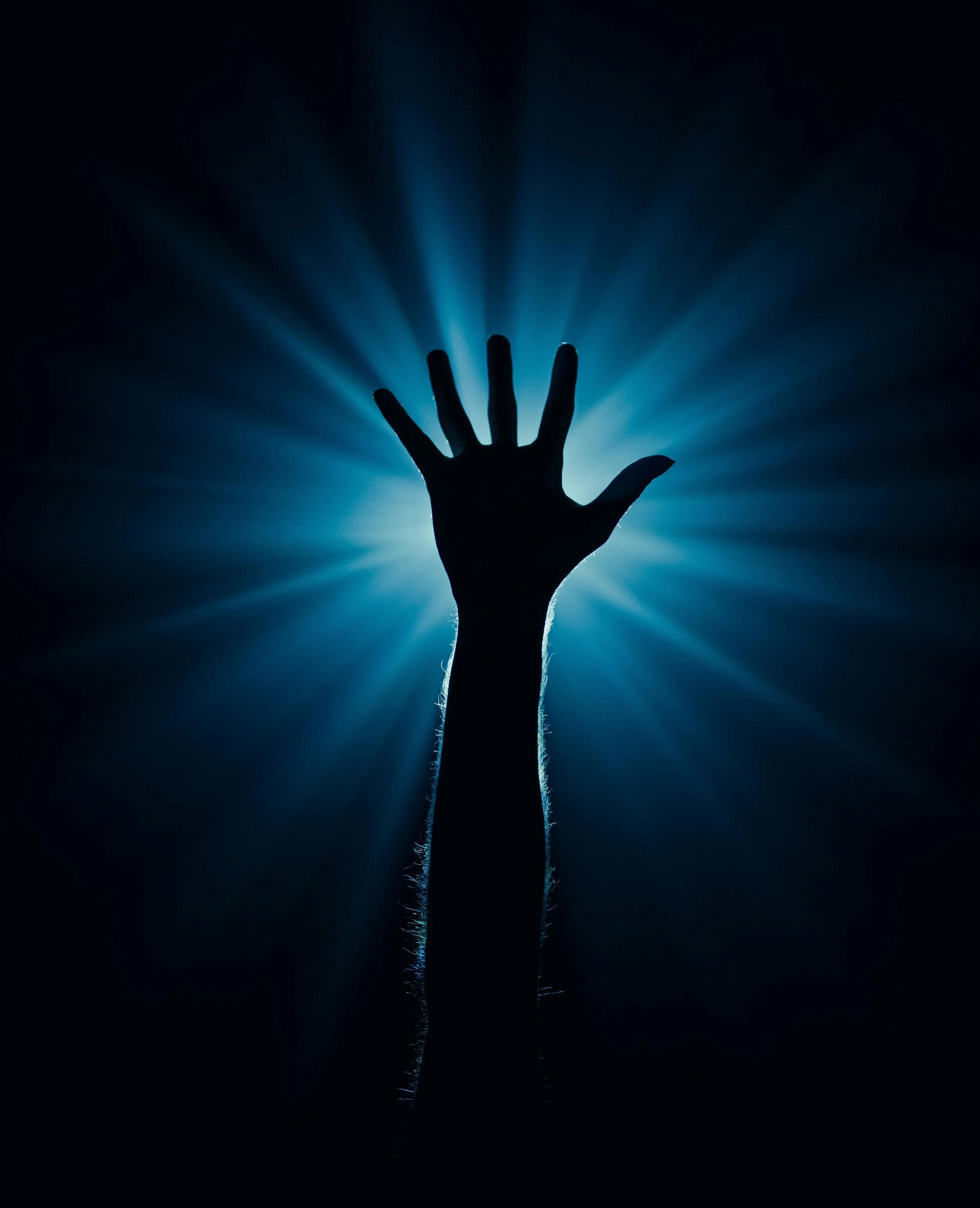 Silhouette of a hand reaching upward against a background of radiant blue light beams.